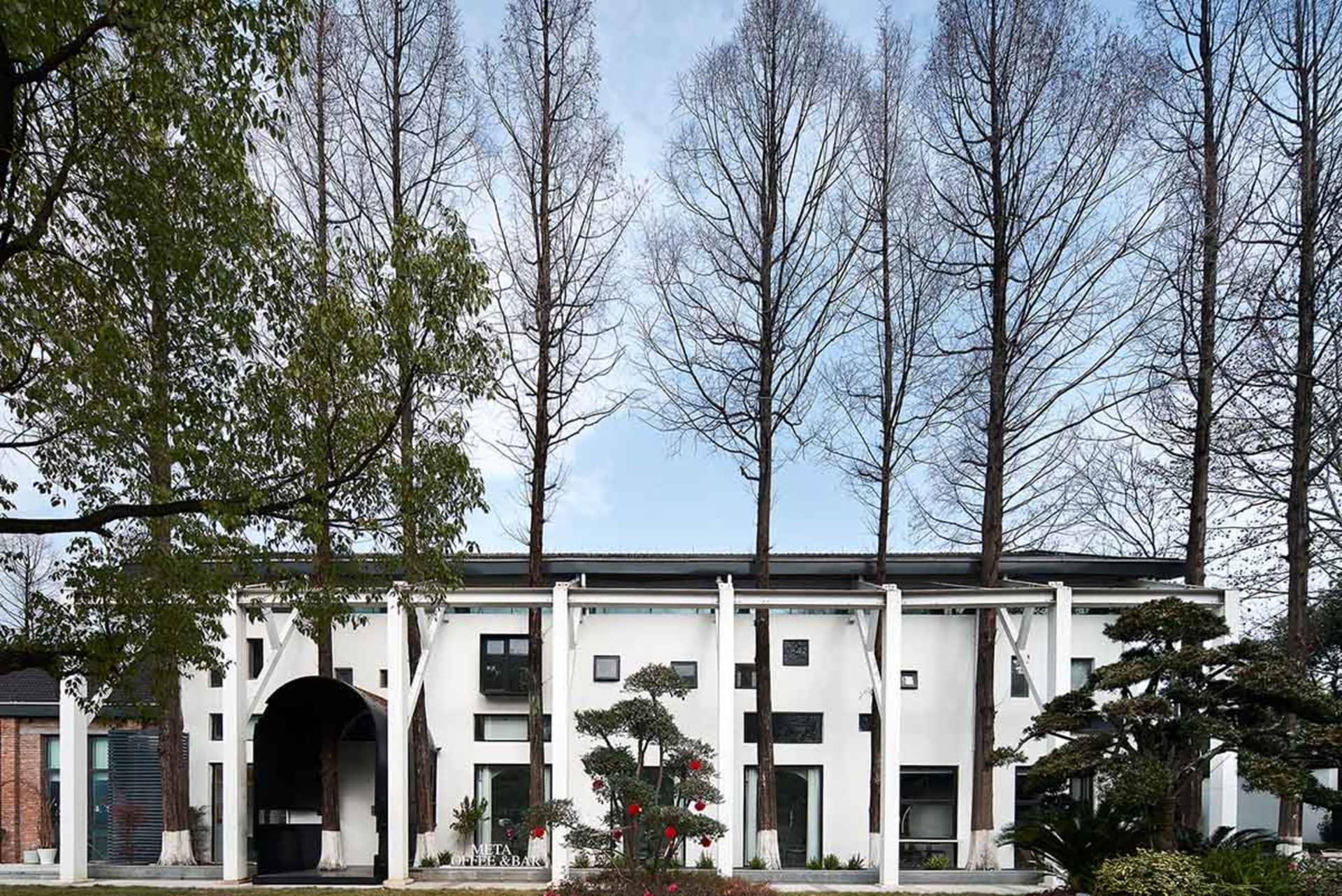 A modern residential building with white paint and concrete exterior, surrounded by greenery and tall trees.