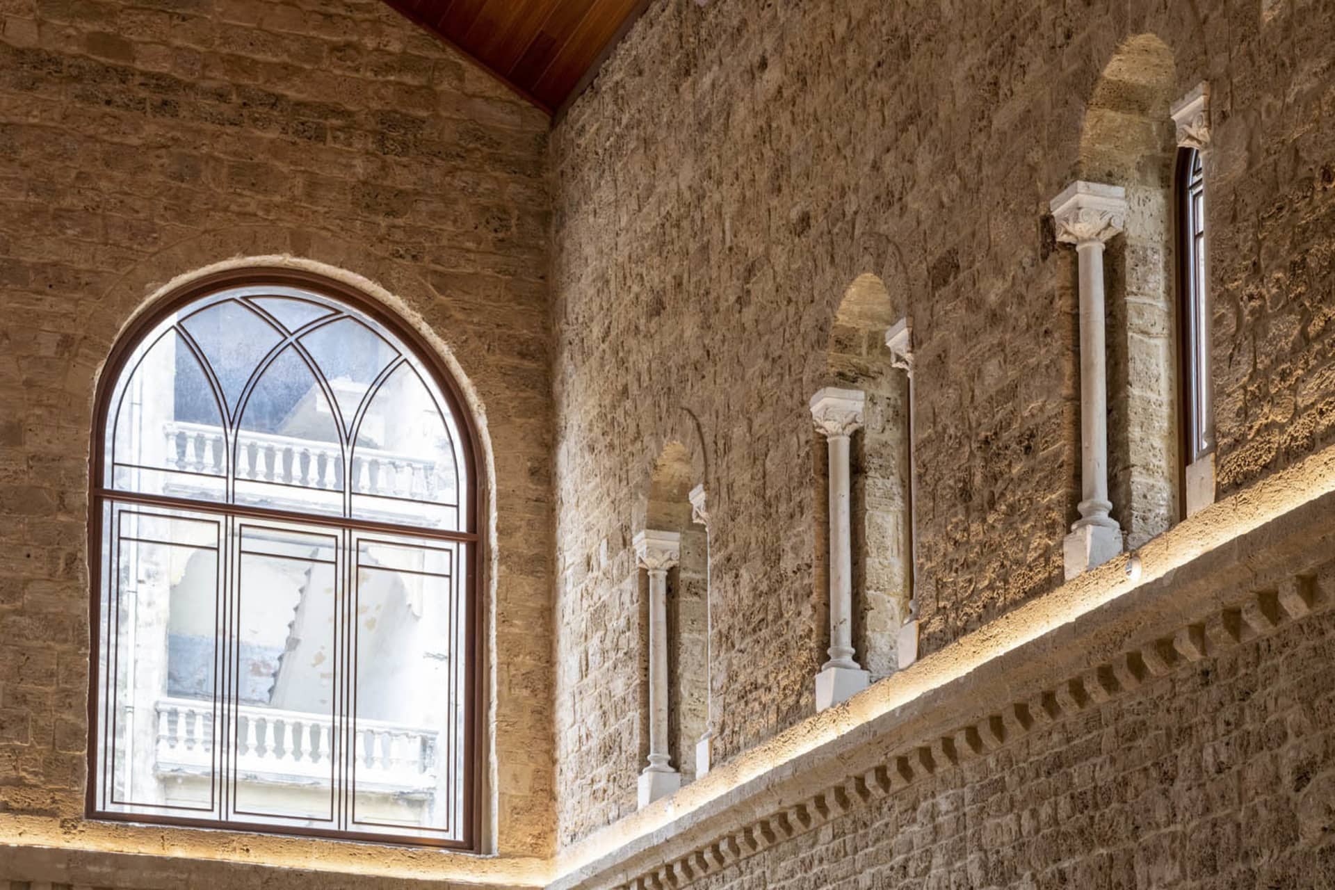 A modern interior space with a stone wall featuring a large, arched window.