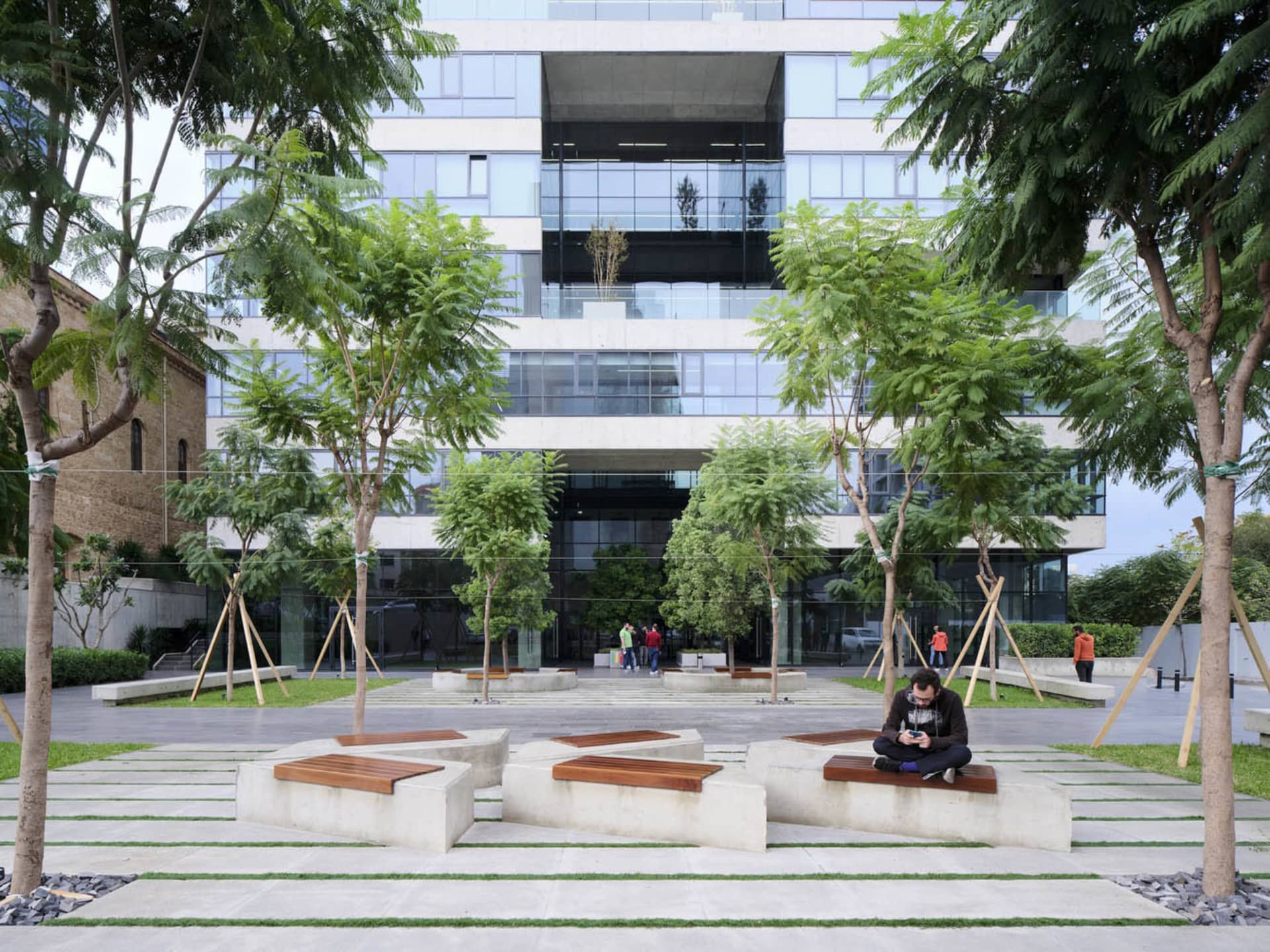 Outdoor urban plaza featuring modern architecture with concrete seating, wooden benches, and glass buildings.