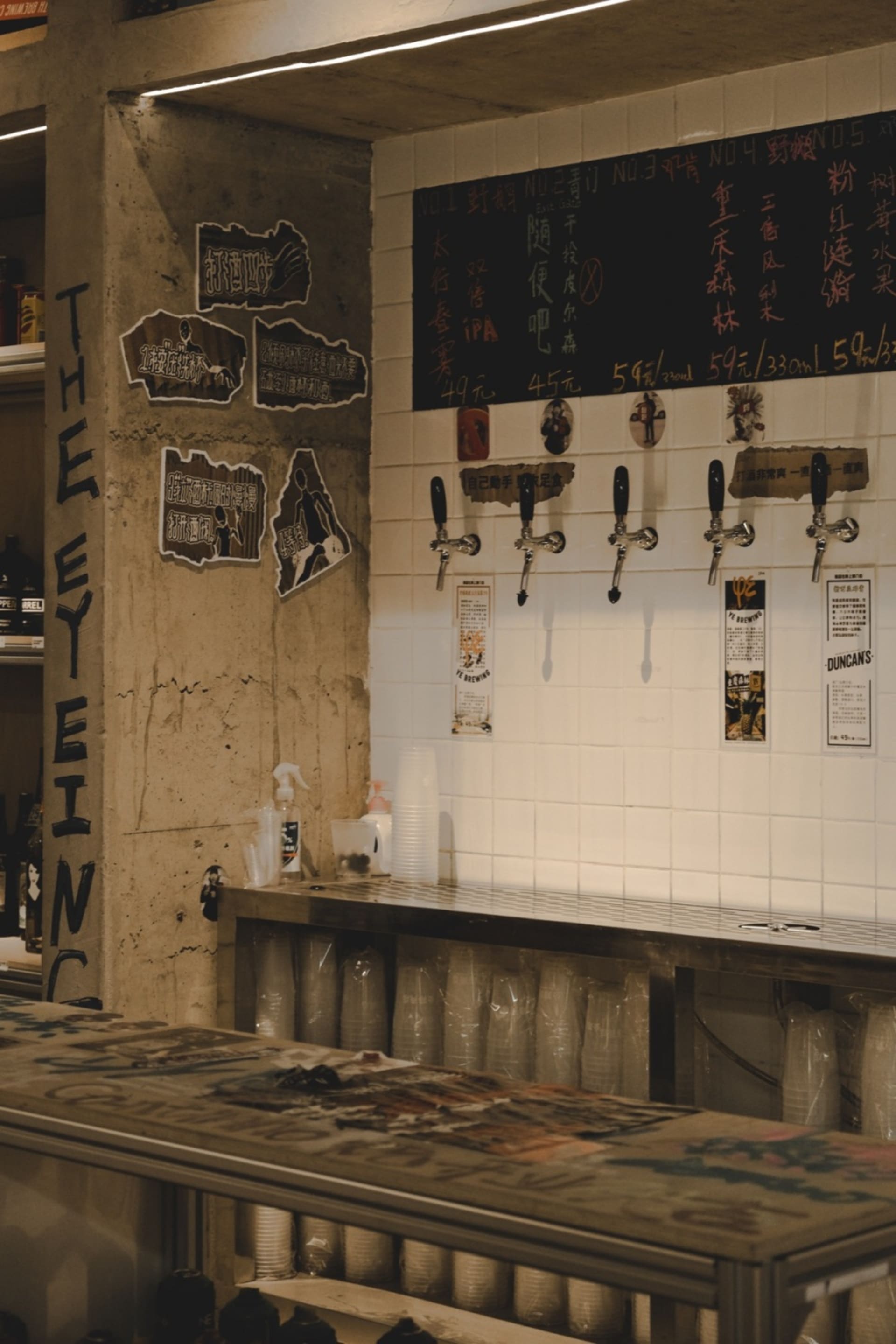 Industrial-style bar interior with concrete walls, metal taps, and a chalkboard menu.