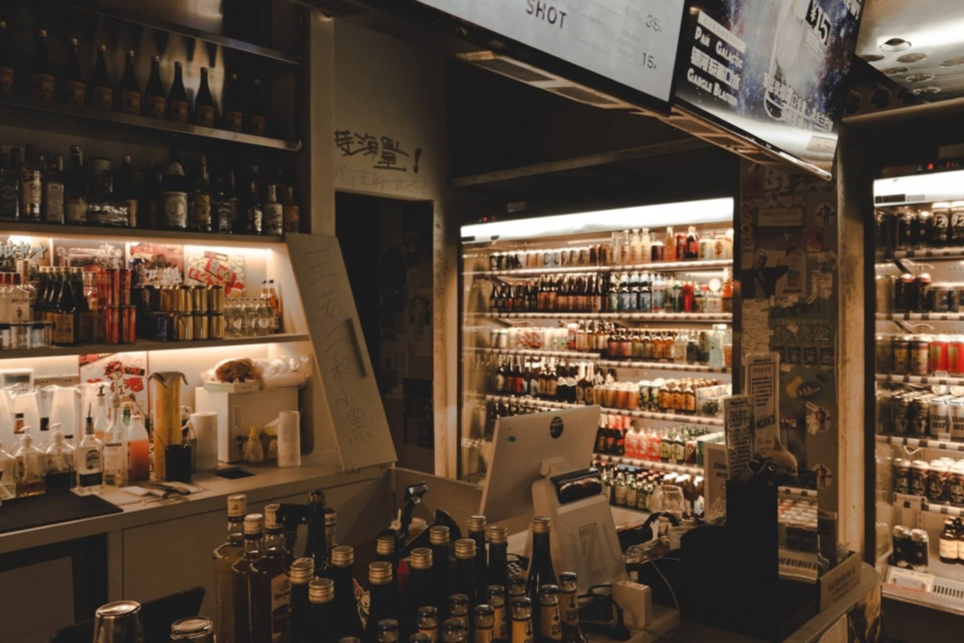 Modern bar with a metallic and glass bar counter on one side and a well-stocked glass shelf on the other, featuring bottles o