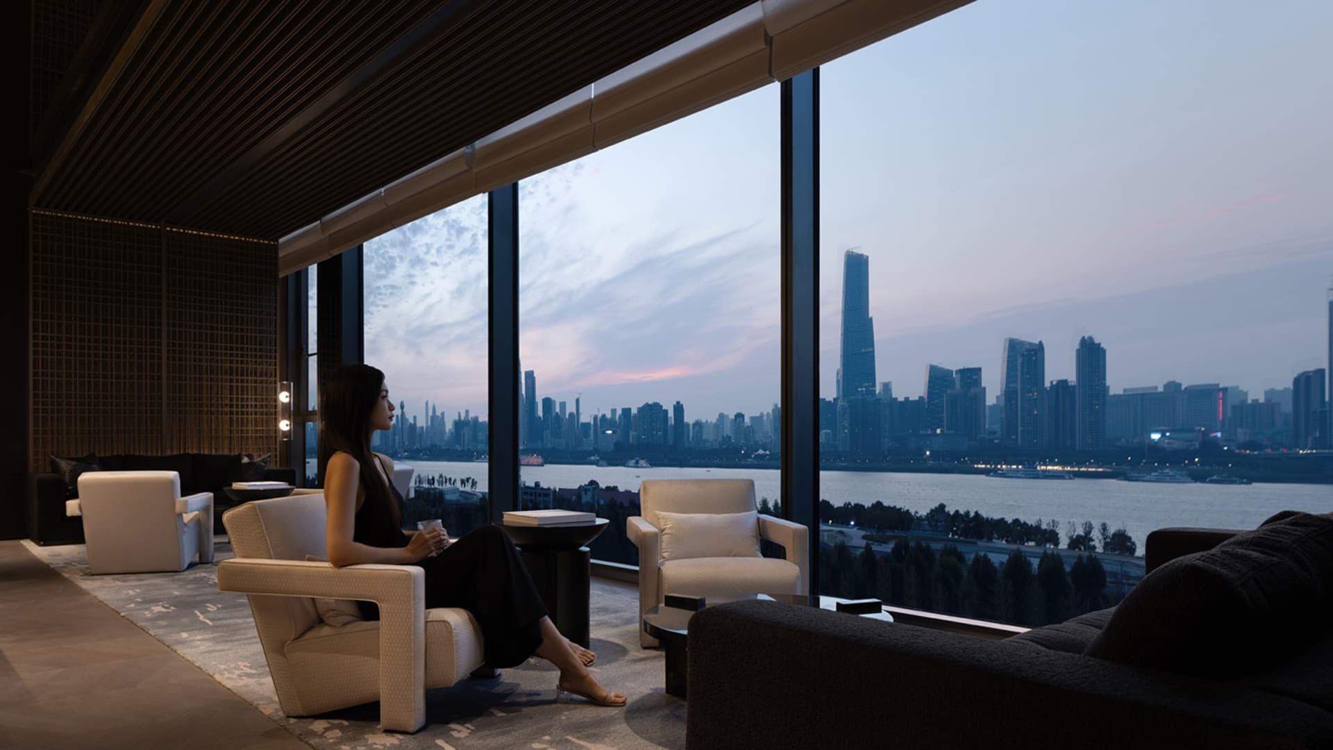 A modern living room with a glass window overlooking a cityscape at sunset.