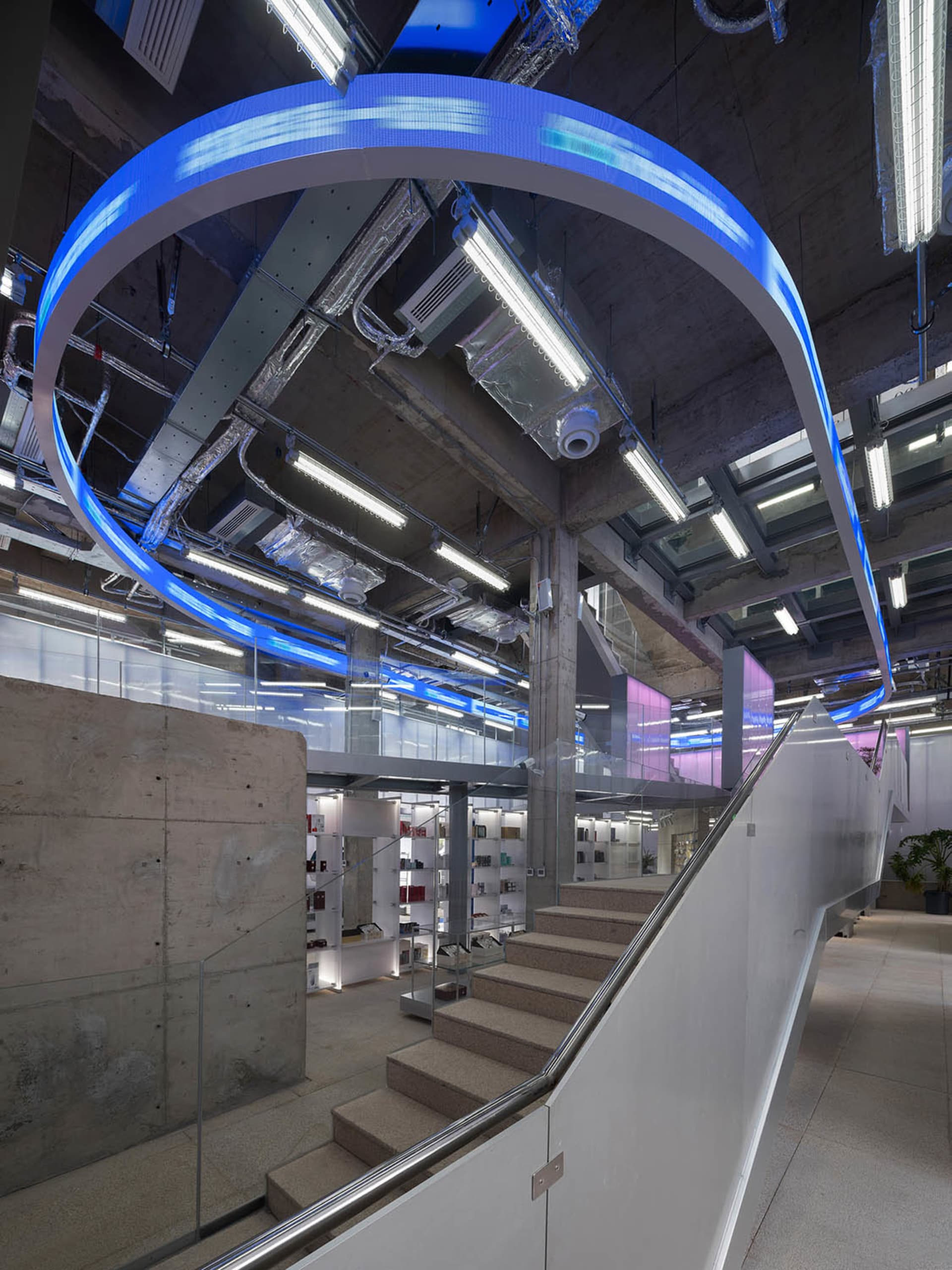 Indoor office space featuring concrete walls, glass walkways, and neon lighting.