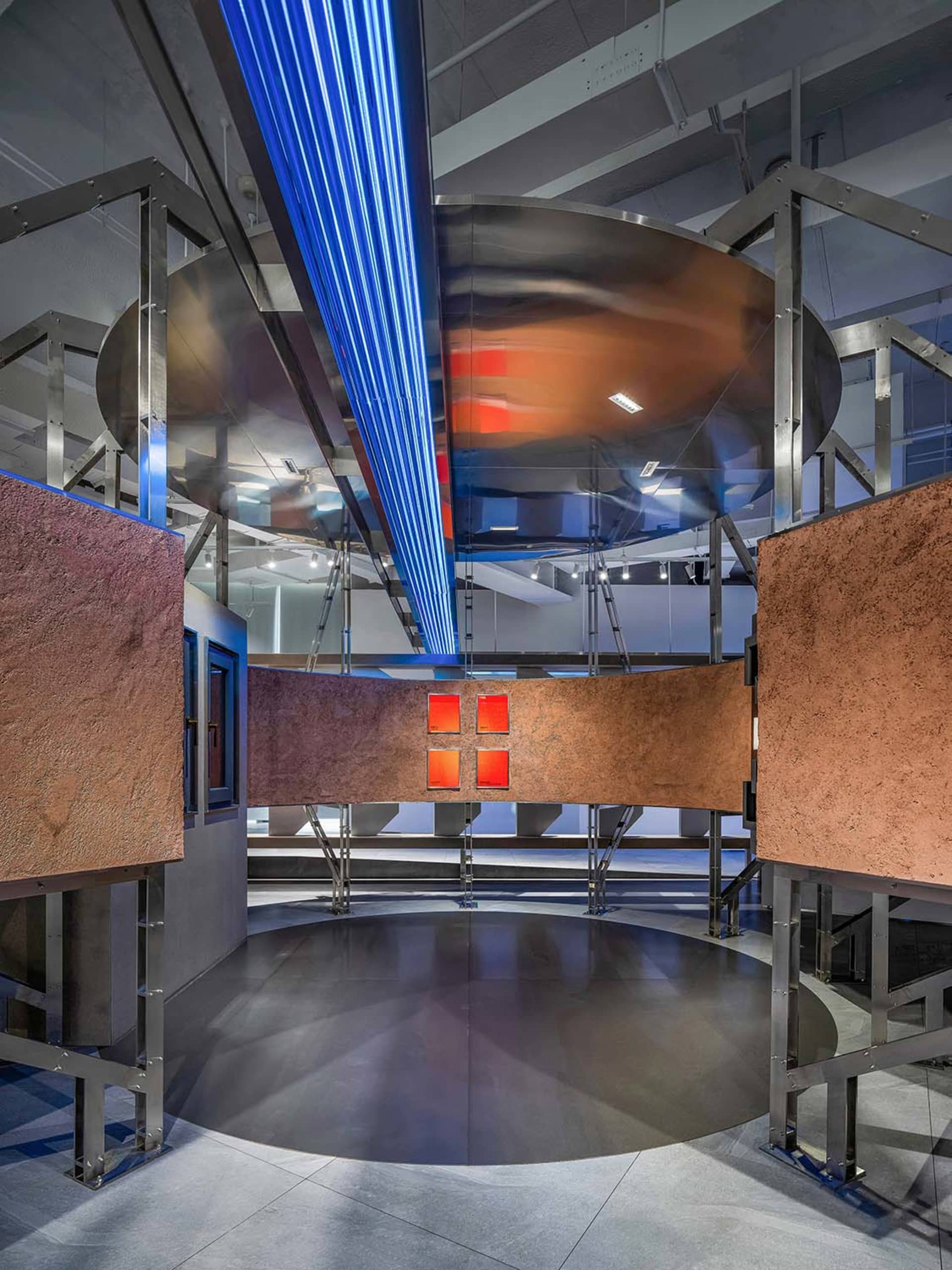 A modern museum exhibition space featuring a reflective metal installation with blue neon lights and red illuminated panels.