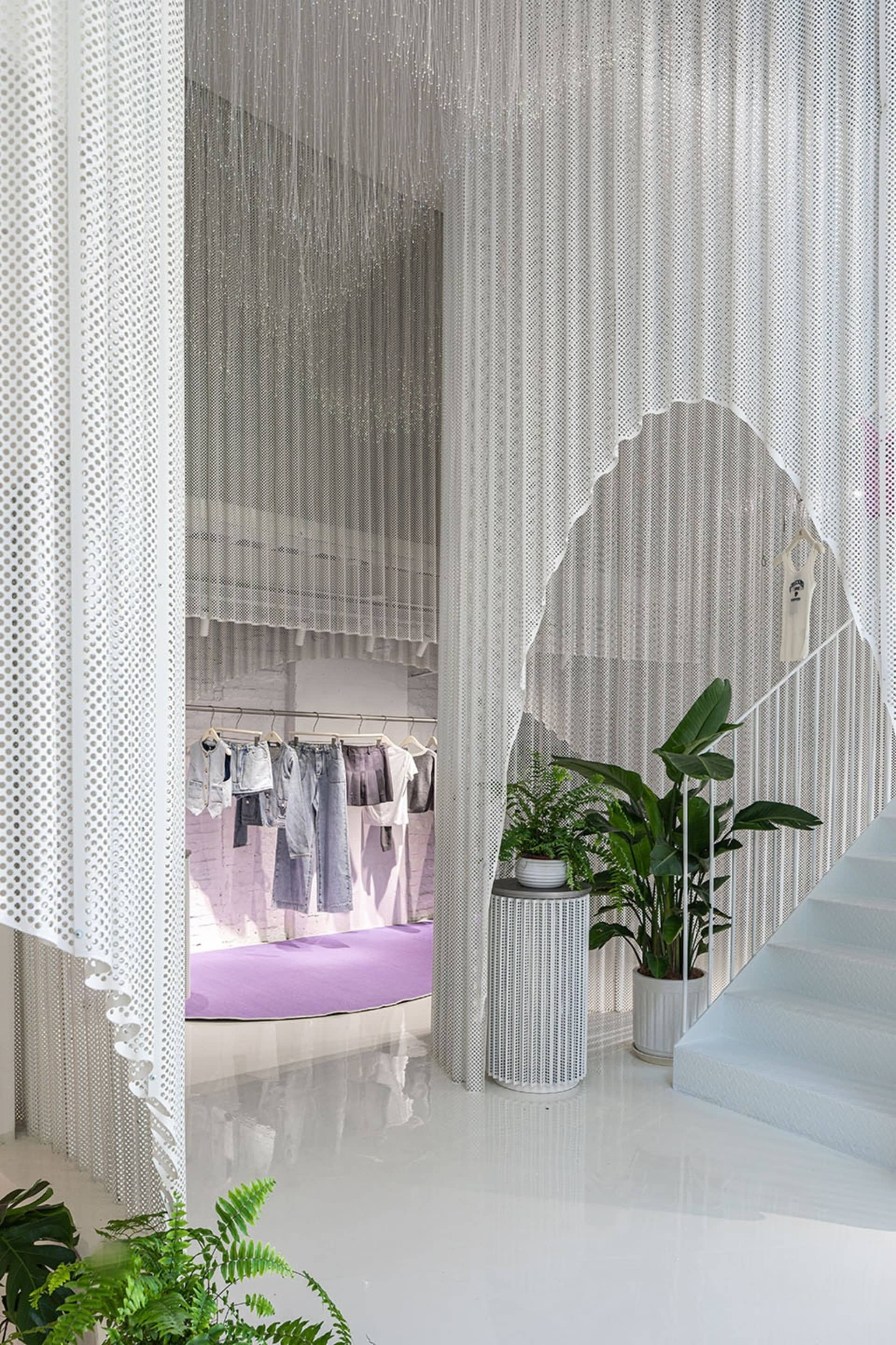 Modern retail store with a white interior, metal perforated screens, and green plants.