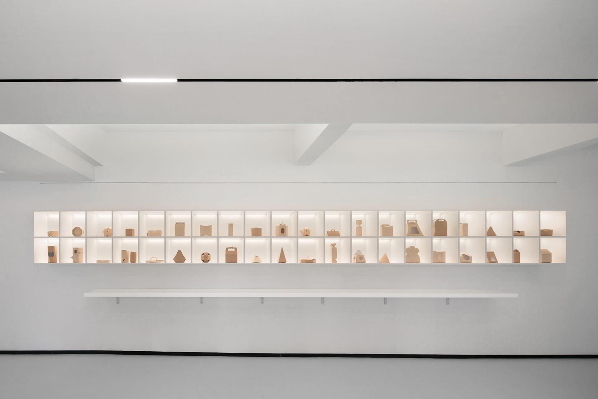 A minimalist art exhibit featuring various paper sculptures displayed on illuminated shelves.