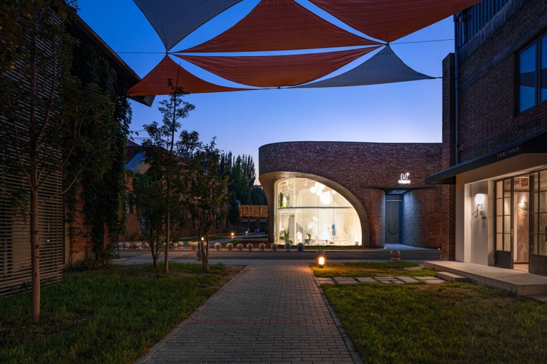 Modern storefront with brick exterior at dusk, featuring a curved glass entrance and large awnings.