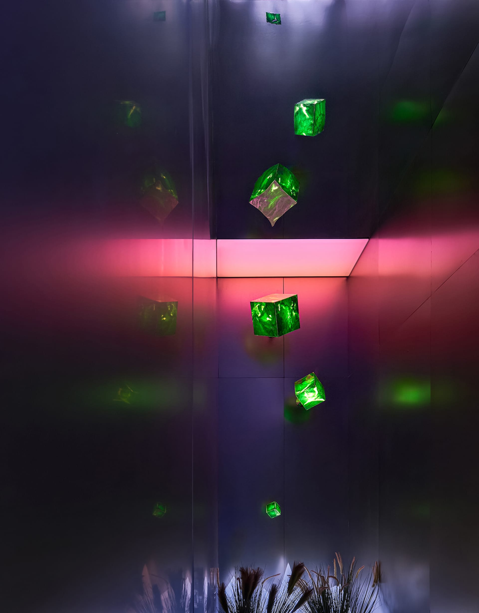 An abstract installation featuring green glass cubes suspended in a dark room with pink and purple lighting.