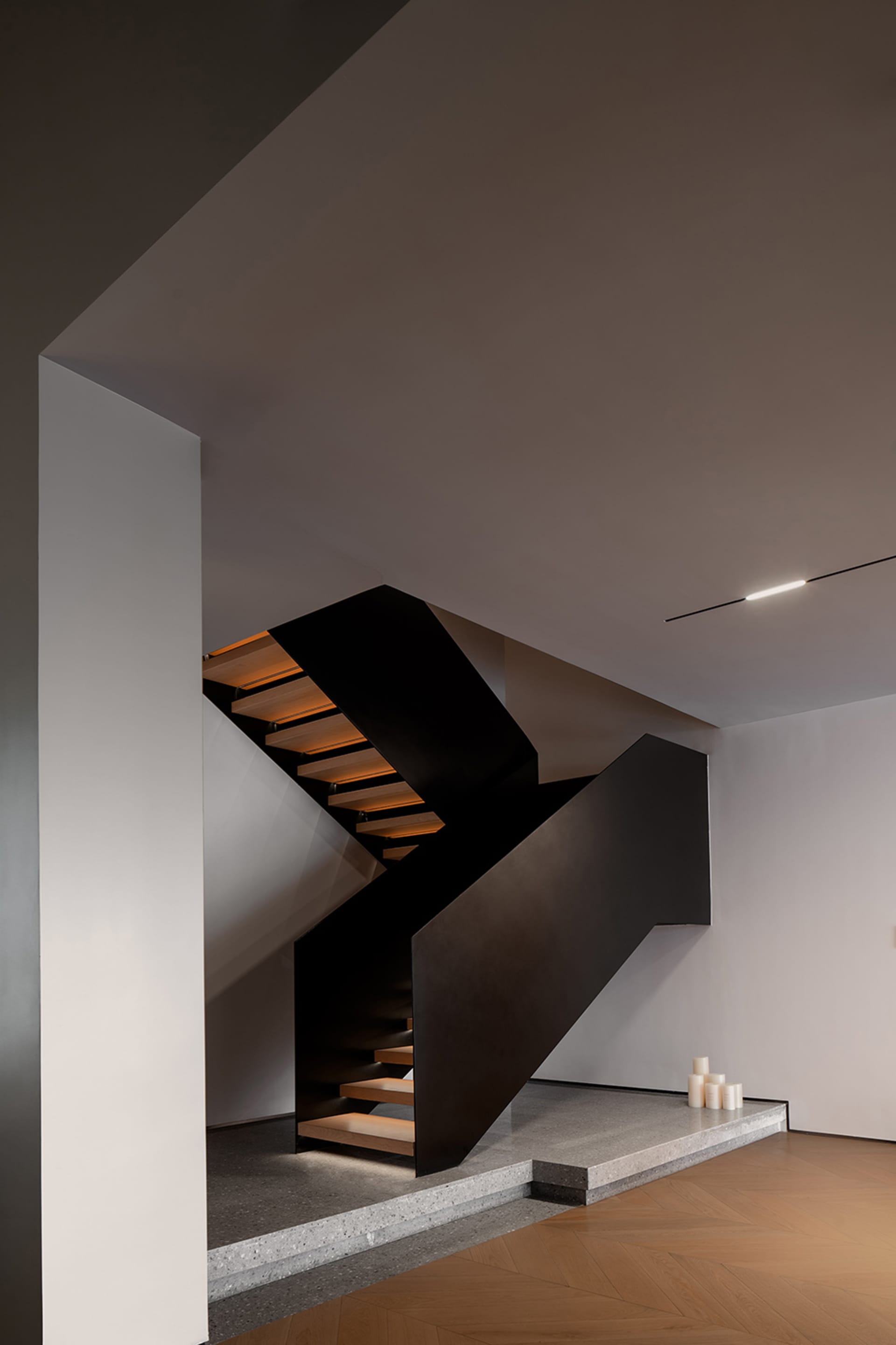 Modern staircase with black handrail and wooden steps illuminated by soft lighting.