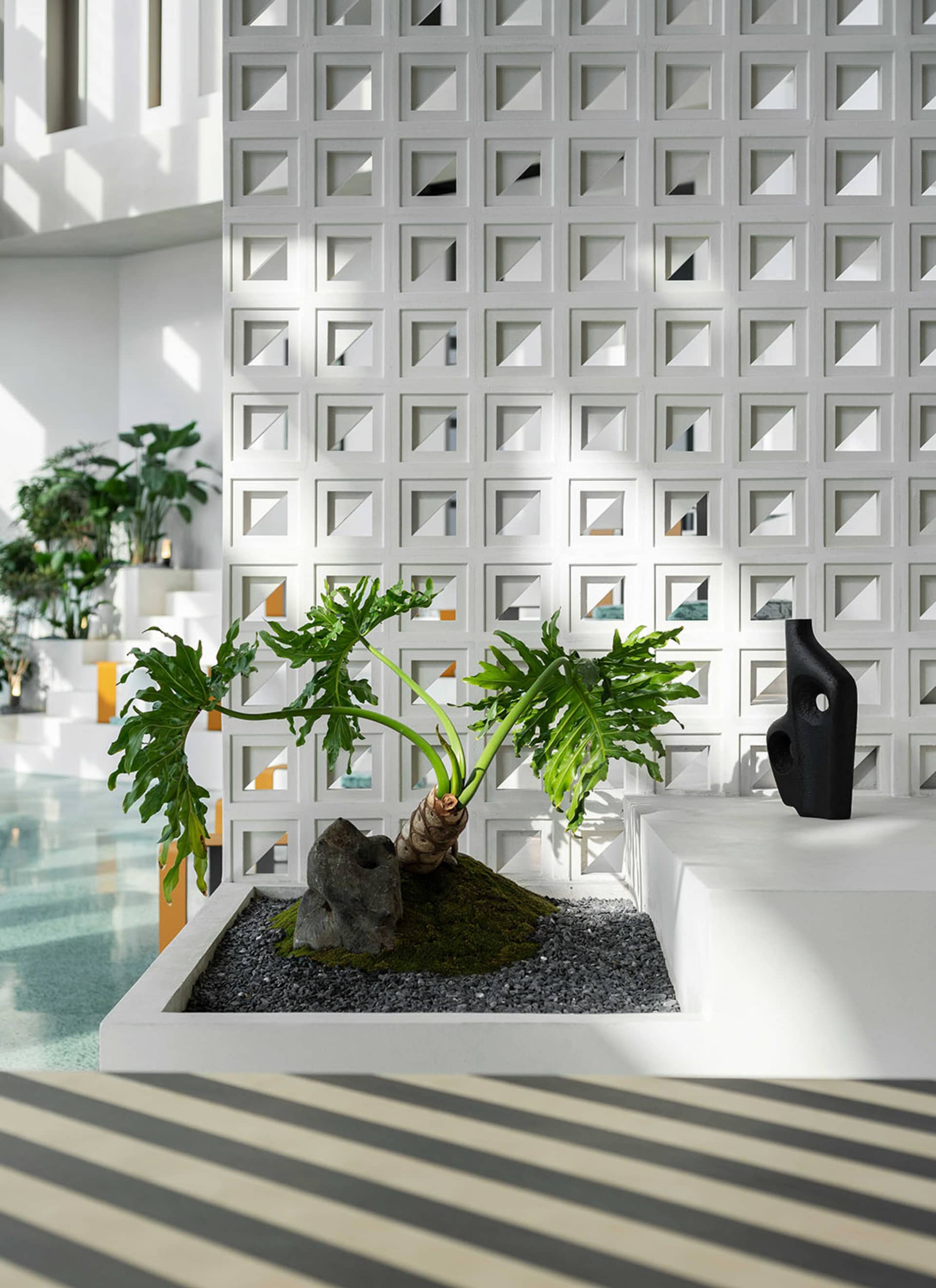 現代建築空間內,一座混凝土與苔蘚邊框的植栽盆,種植綠色植物,並搭配黑色抽象雕塑。