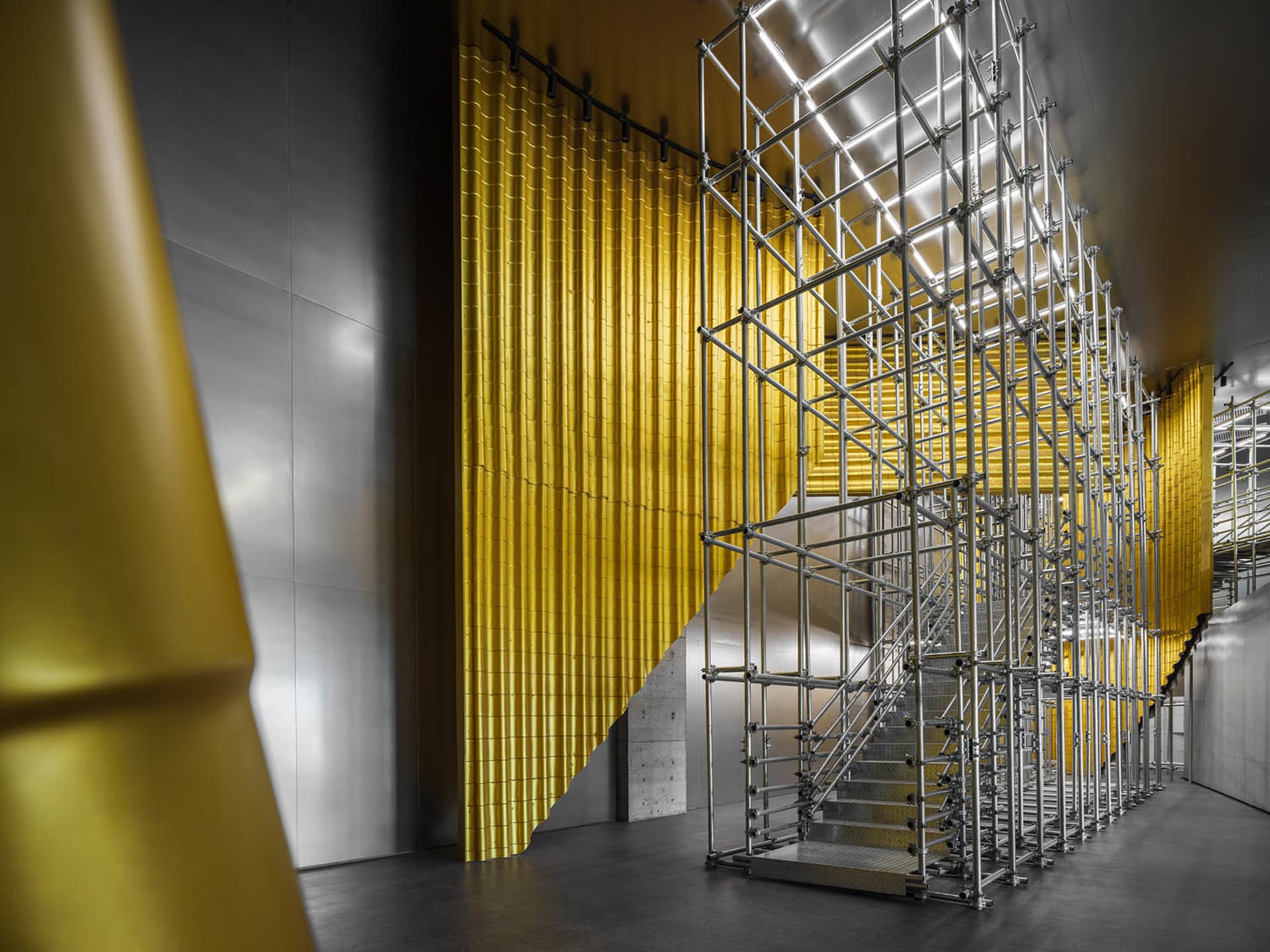 Metal scaffolding structure with yellow metal elements in an industrial interior setting.