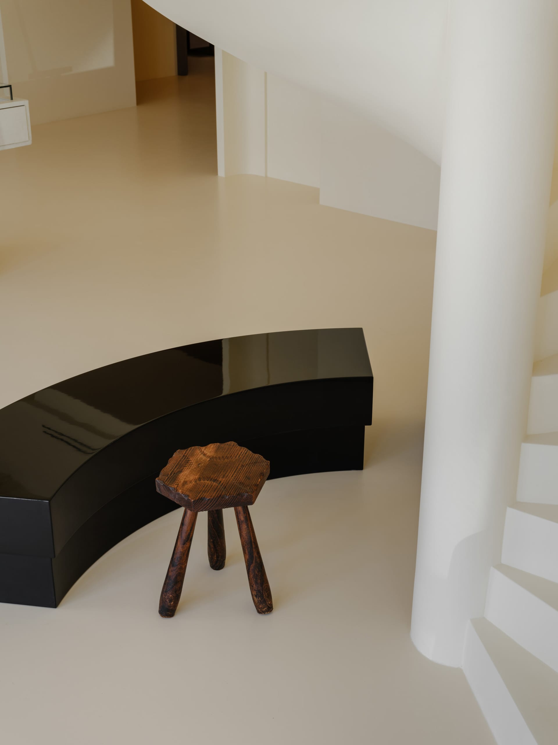 A minimalist room with a black curved bench and wooden stool, featuring modern interior design elements.