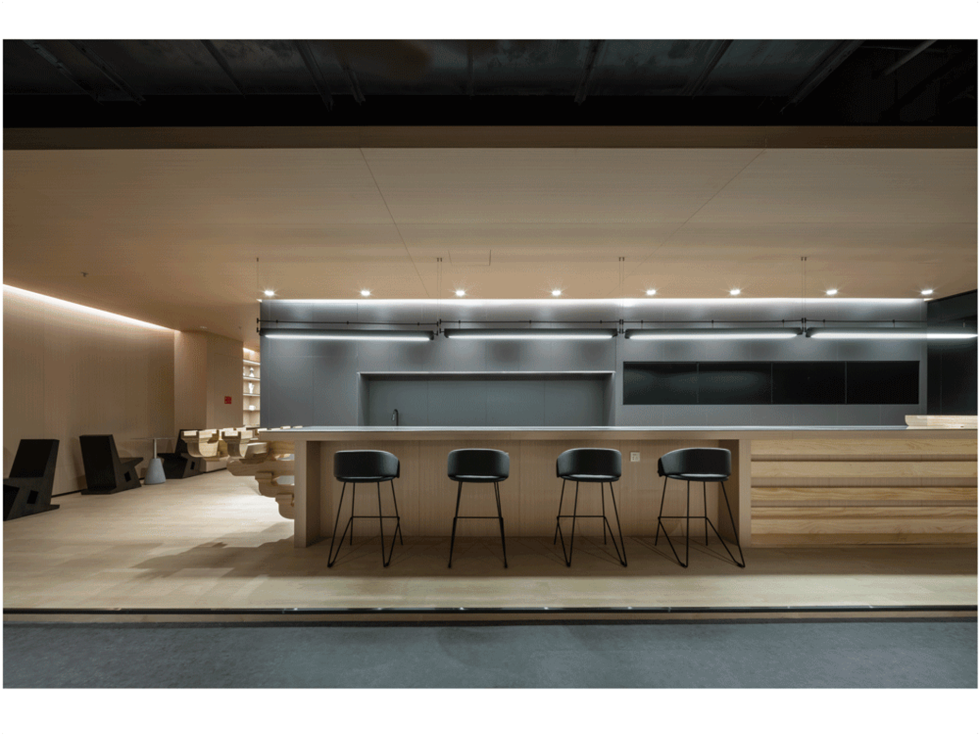 Industrial-style bar counter with four wooden bar stools under a modern lighting fixture.