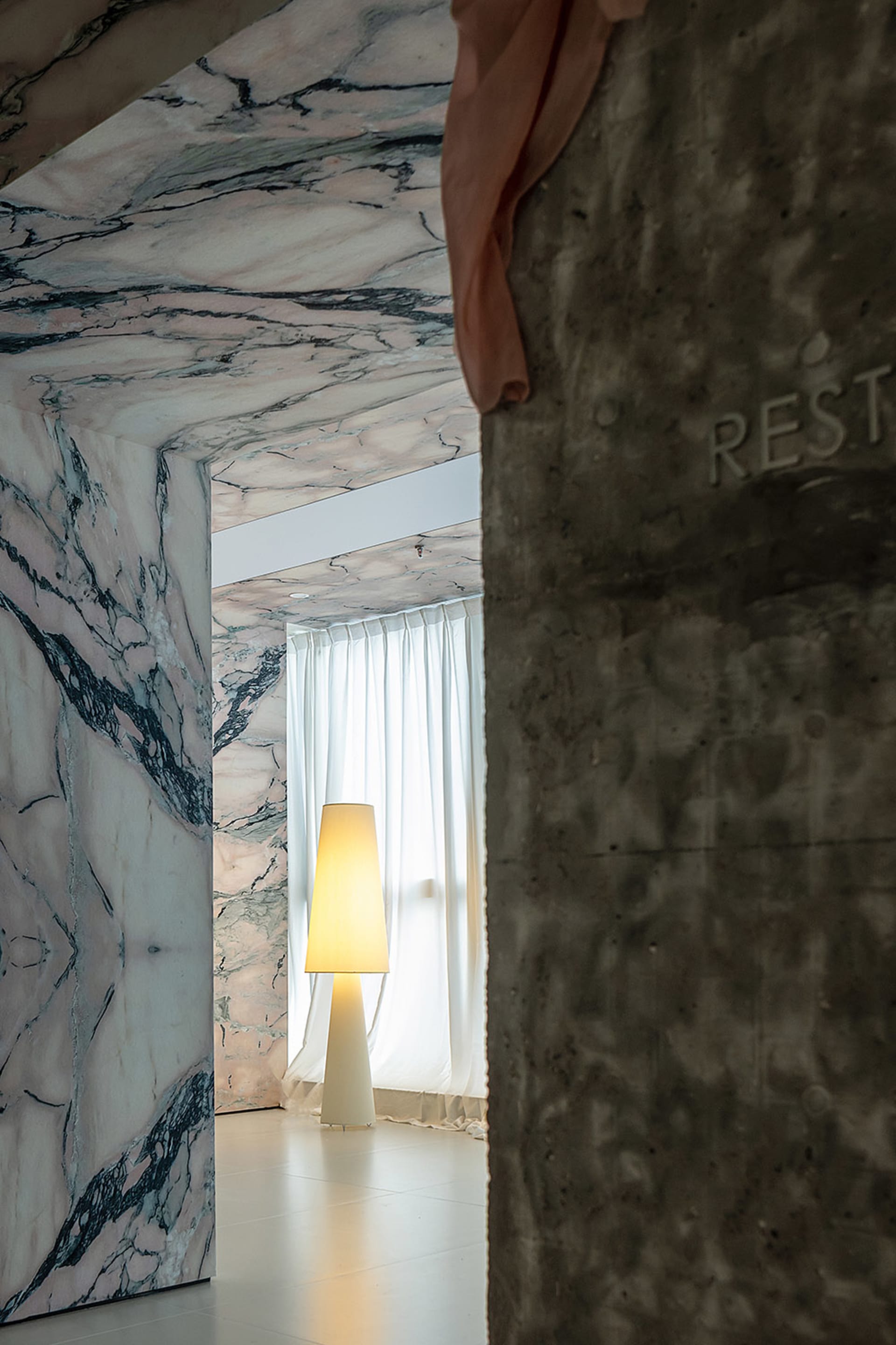A minimalist interior space featuring marble walls and a concrete pillar.