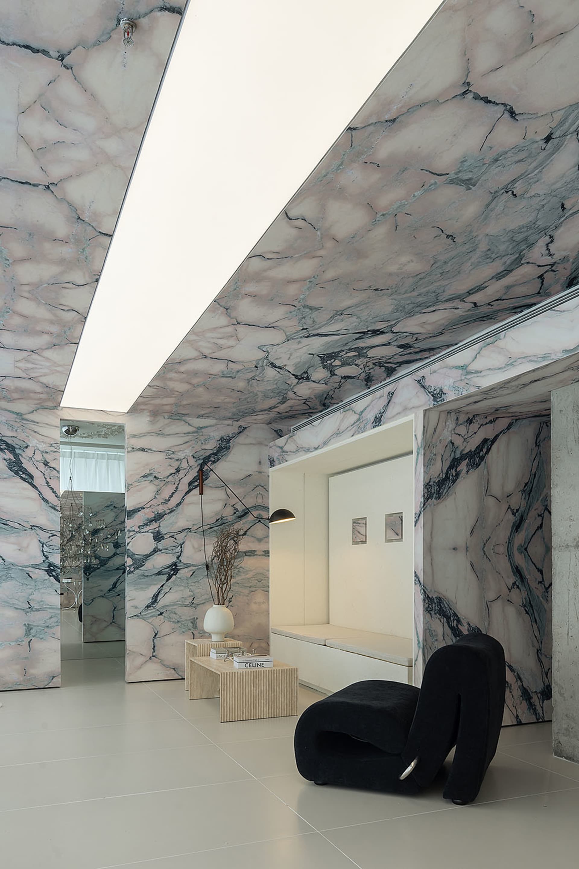 A contemporary living area featuring luxurious marble walls and ceiling, with sleek black furniture and minimalist decor.