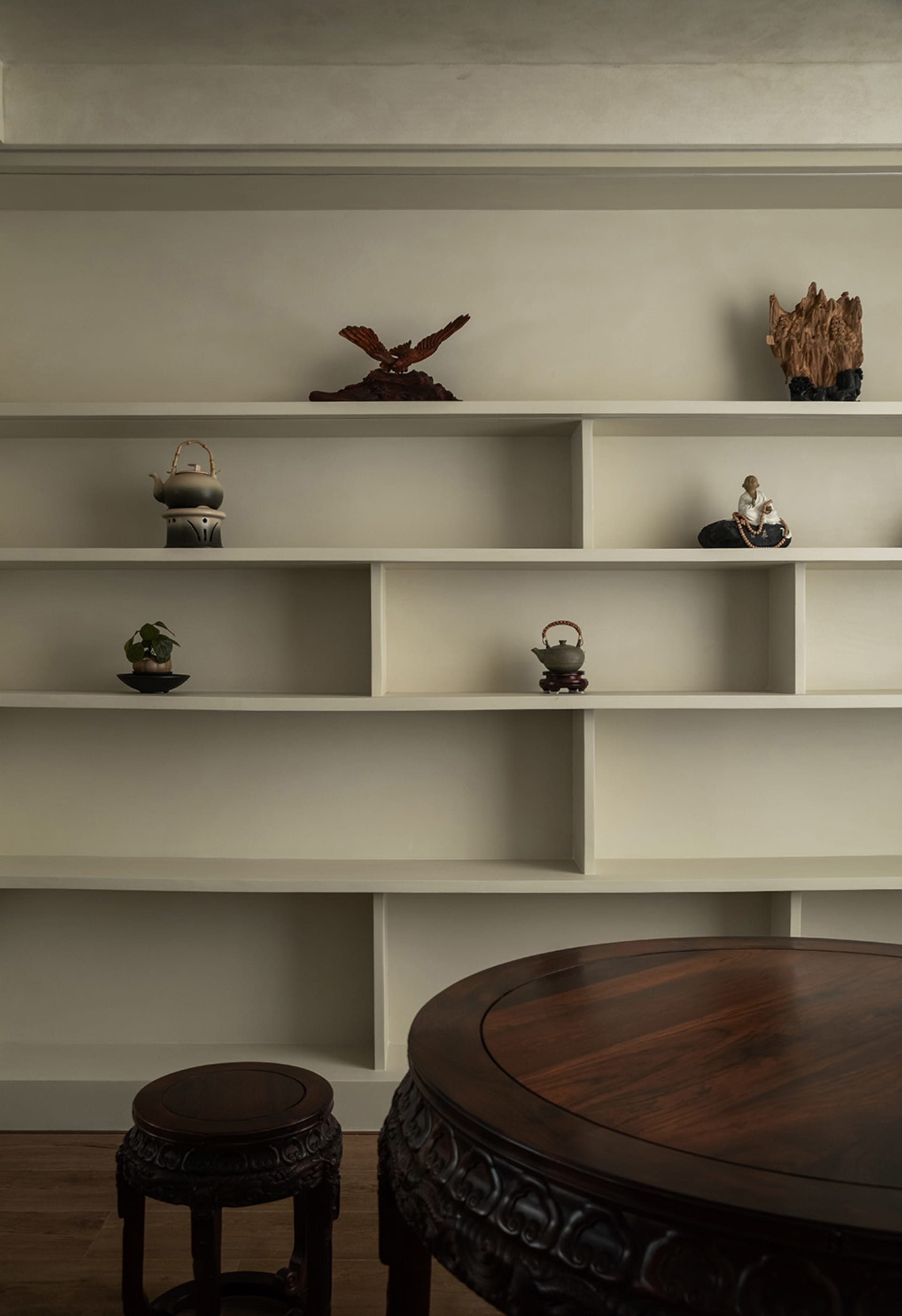 A minimalist living room featuring a white bookshelf with various decorative items and a wooden table.