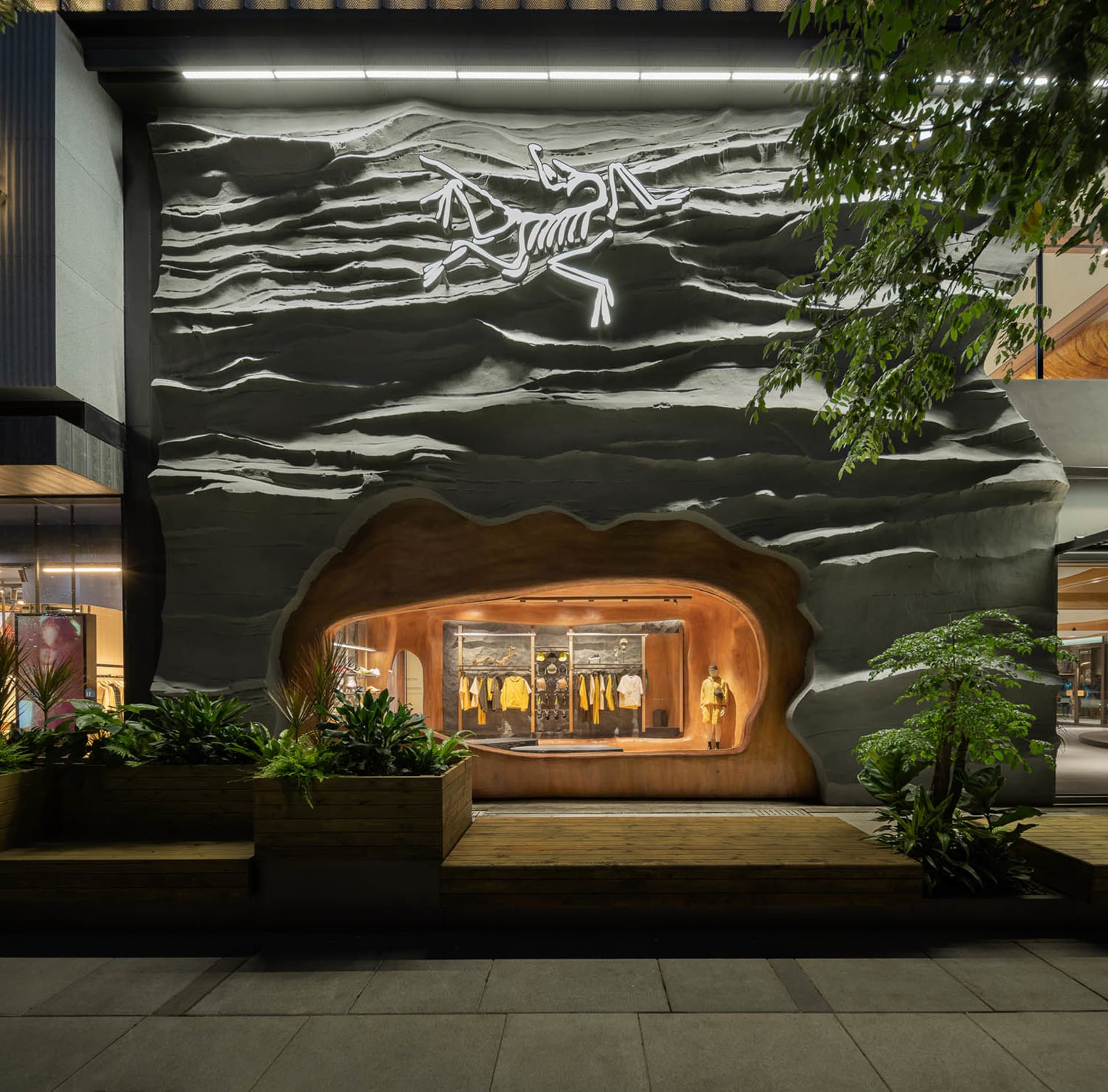 A modern storefront with a textured wall featuring a bird emblem and illuminated clothing display.