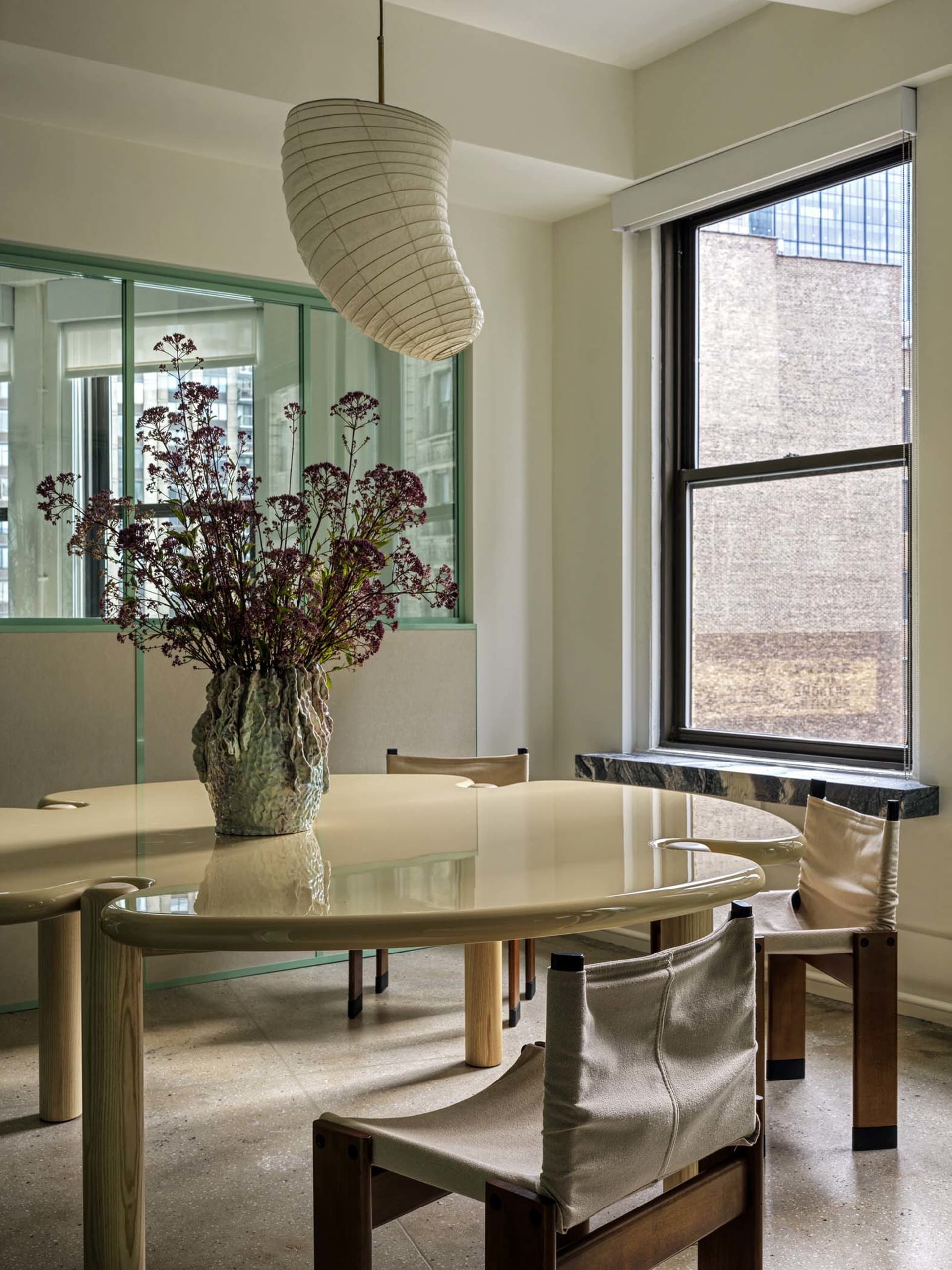 Modern dining room featuring a round glass table surrounded by wooden chairs and a hanging light fixture.