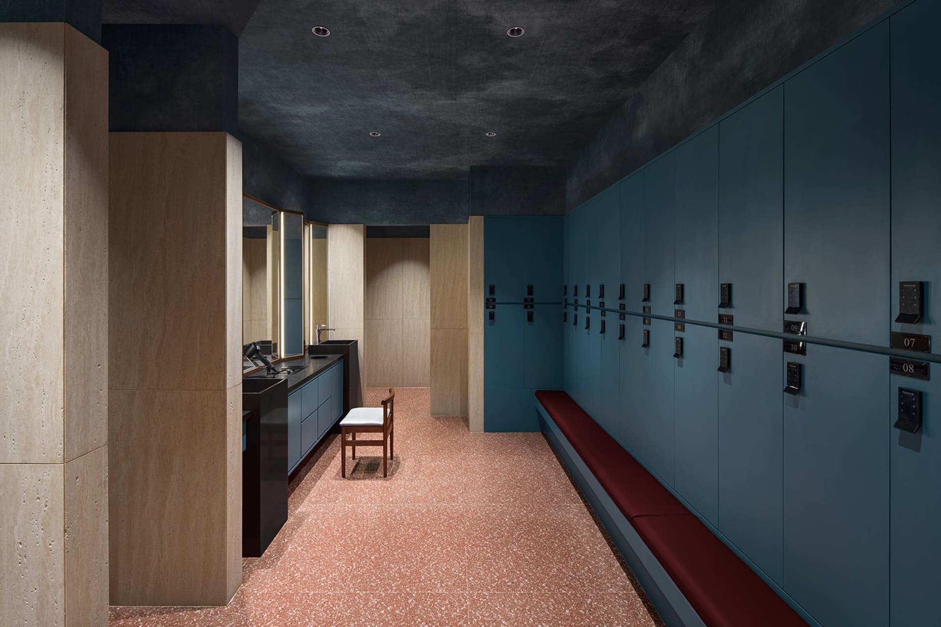 Modern locker room with terrazzo flooring, wooden benches, and metal lockers with numbered keys.