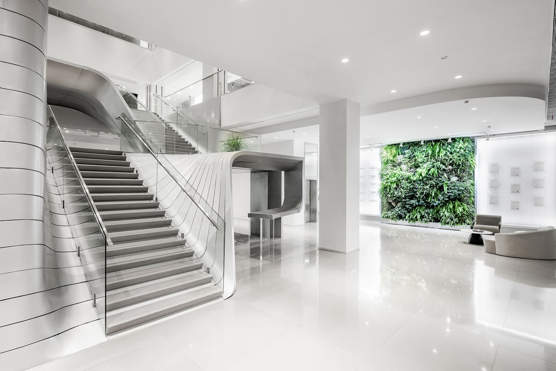 A sleek, minimalist office lobby with modern, white concrete staircase and glass railings.