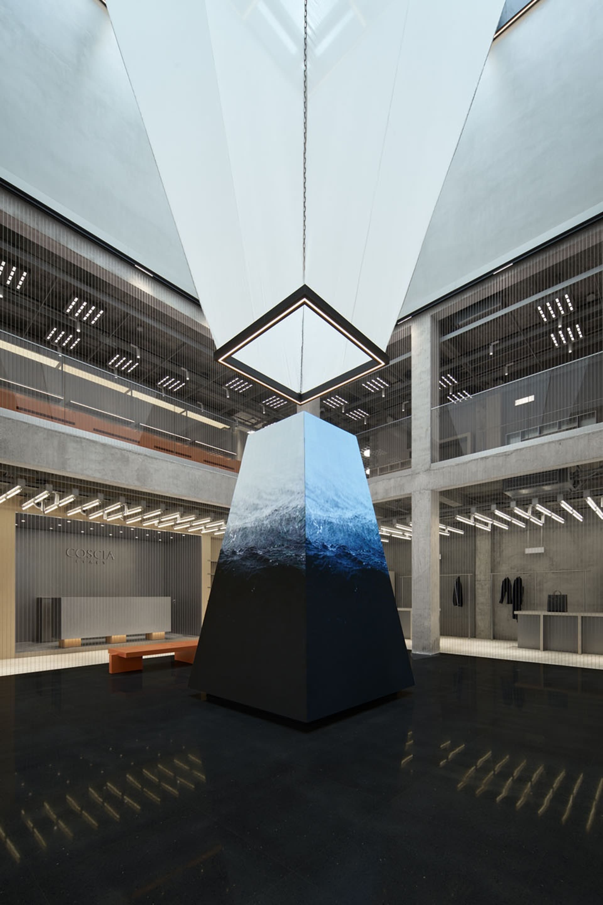 A modern retail interior featuring a large, geometric concrete pyramid structure at its center, surrounded by extensive glass