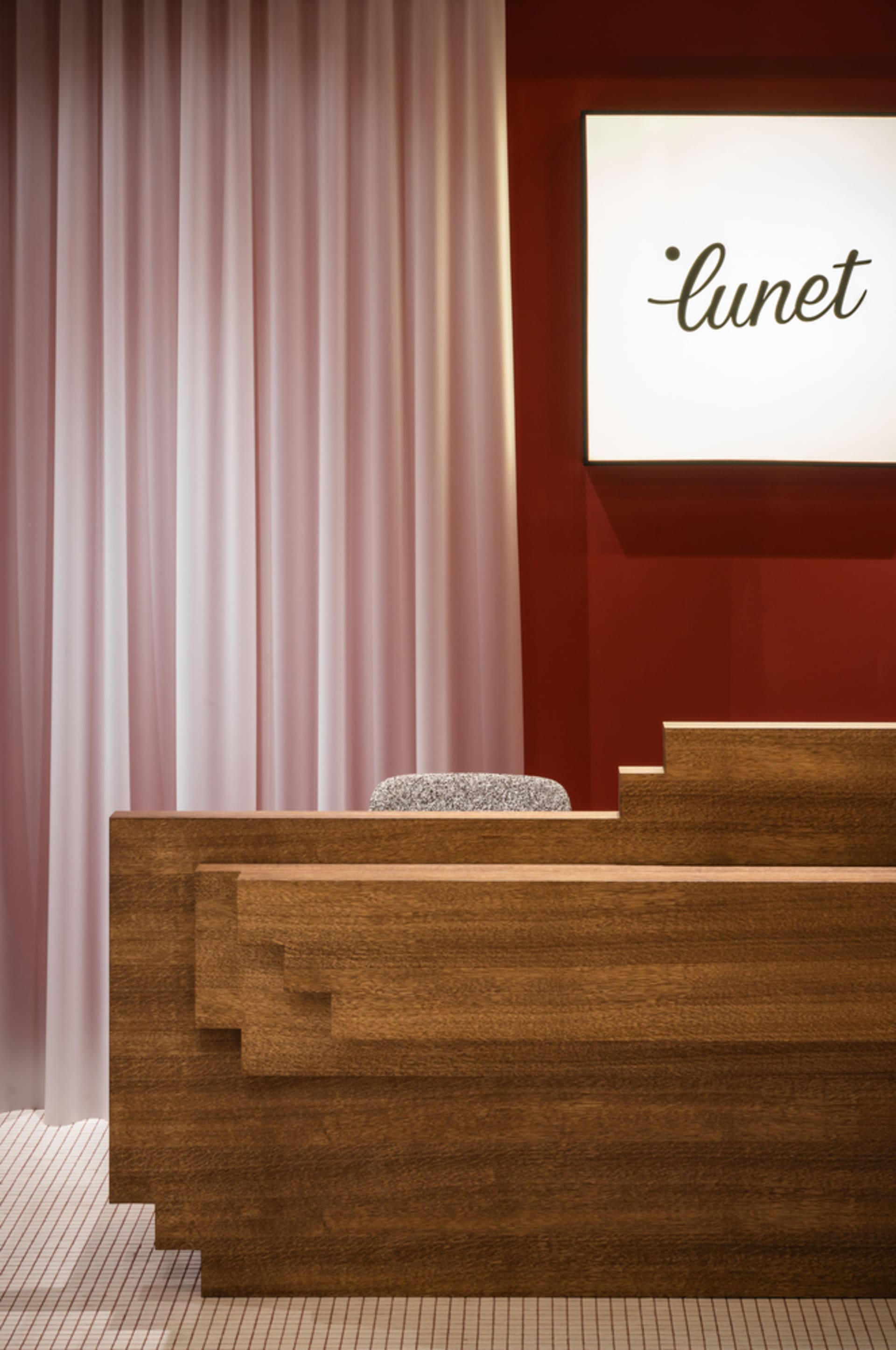 Modern interior design featuring a wooden reception desk with a pink curtain and a red wall.