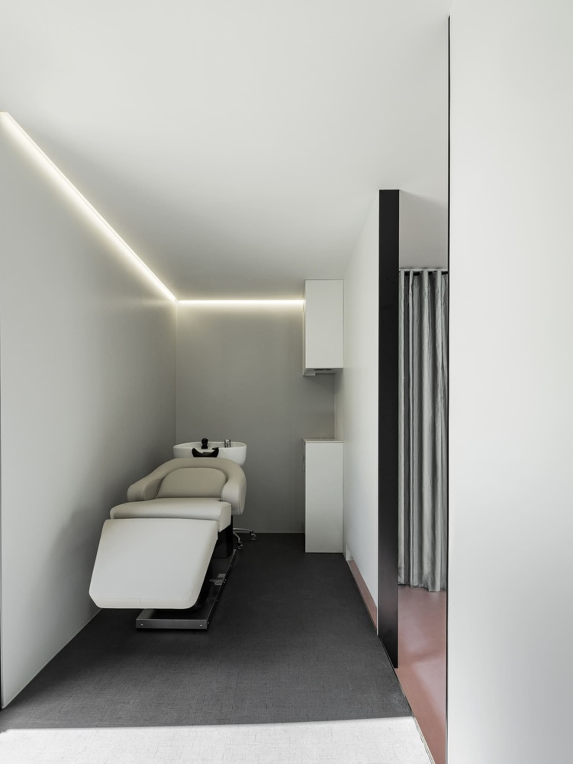 A modern interior spa treatment room with white walls, black flooring, and minimalist design elements.