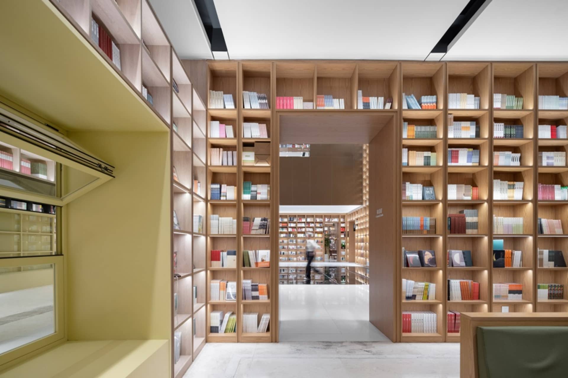 A modern library with a minimalist design and wooden shelves filled with books.