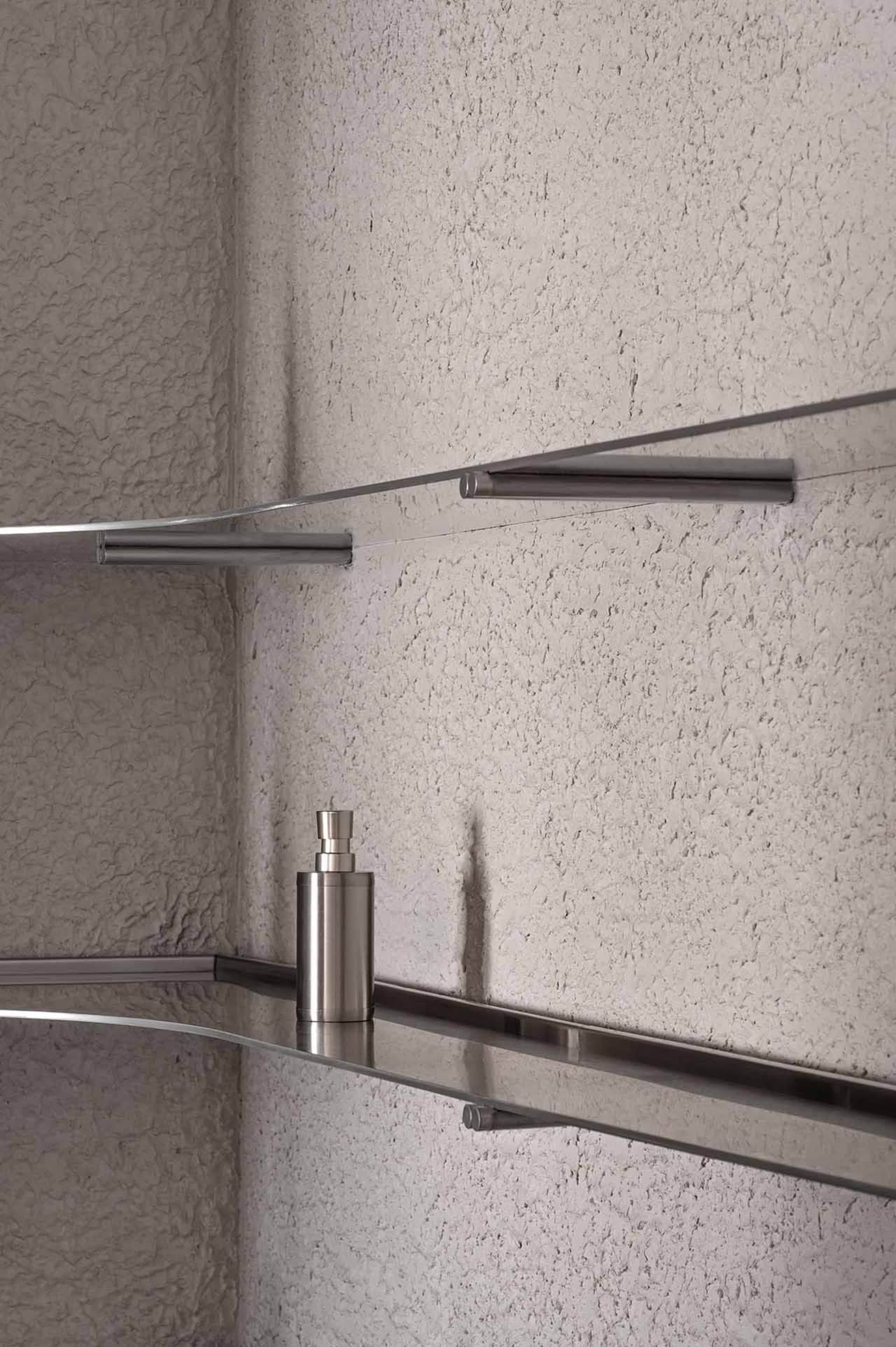 Modern metal shelves with glass surfaces against a textured wall.