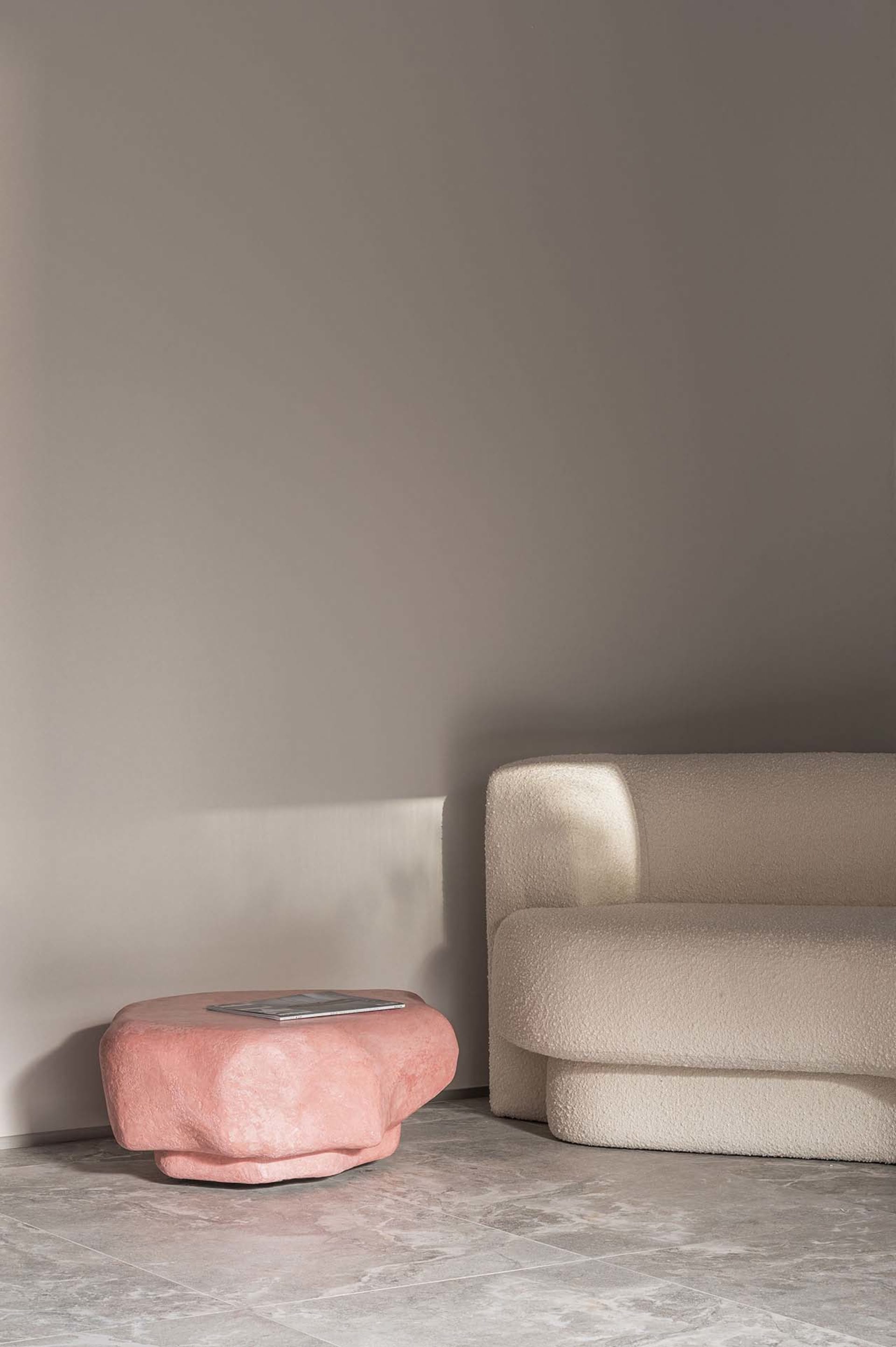 A modern sofa with a plush, white boucle upholstery paired with a pink, organic-shaped side table.