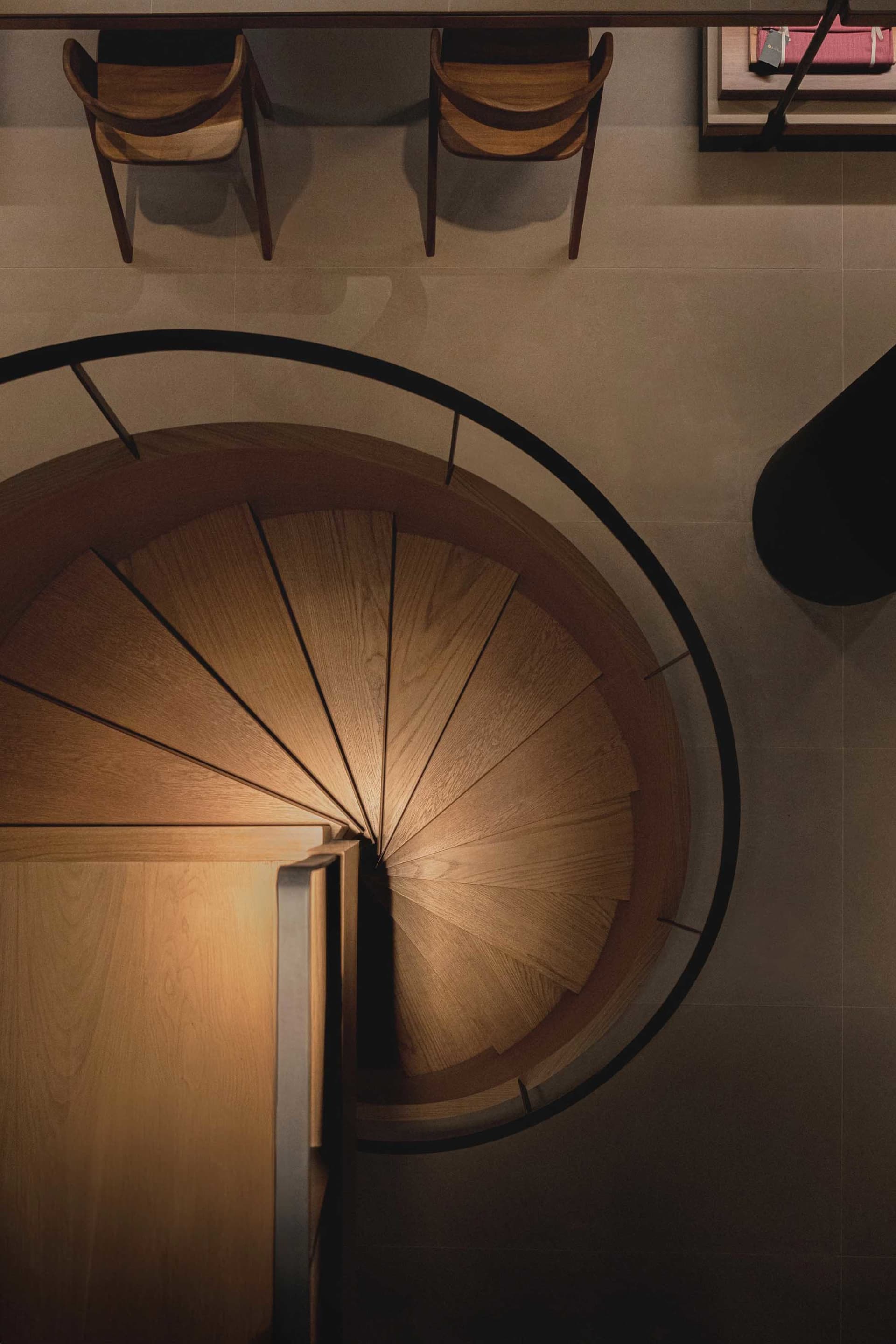 A modern wooden staircase with black railings viewed from above, showing the spiral design and landing.