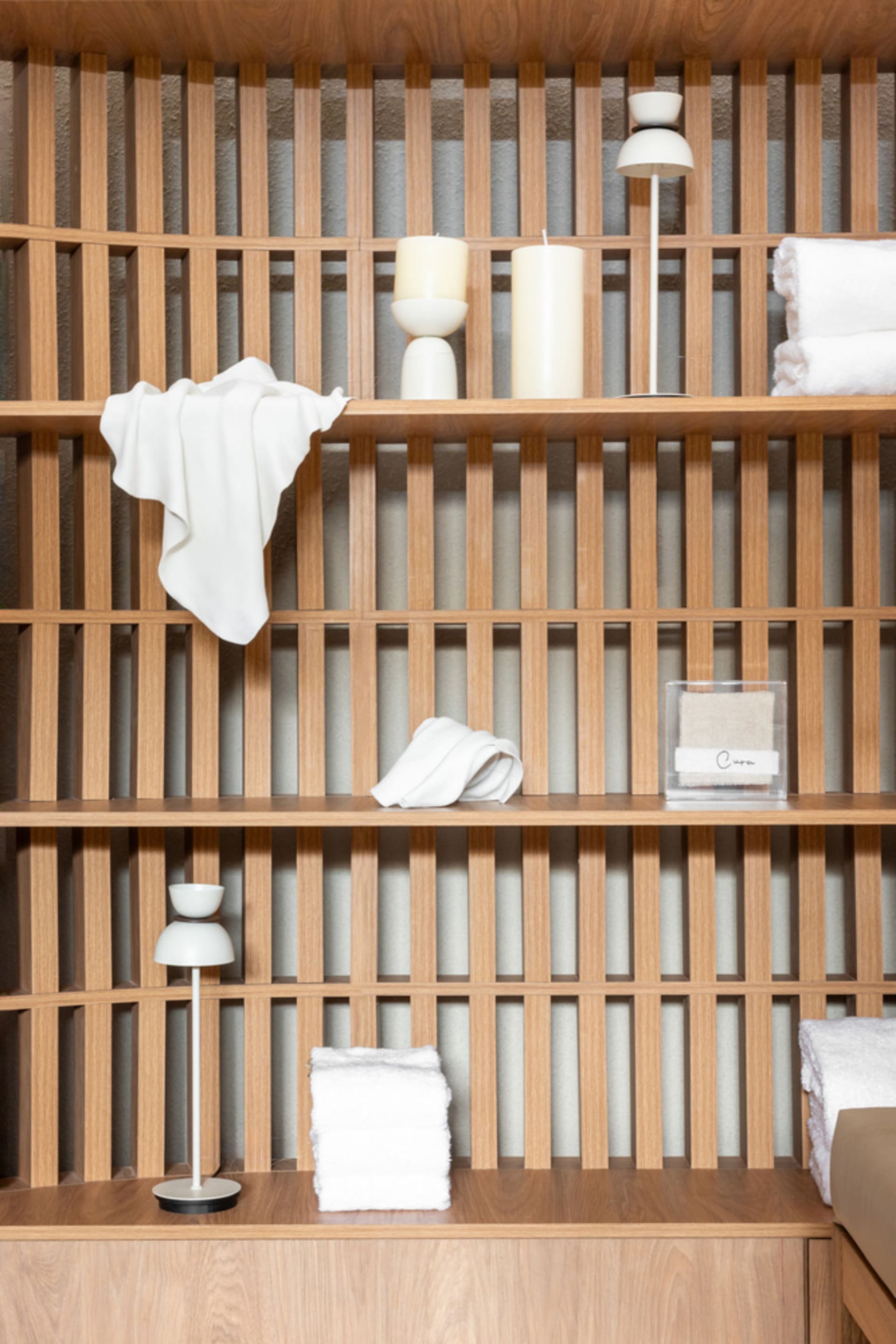 A minimalist shelf made of wood, featuring white towels and candles.