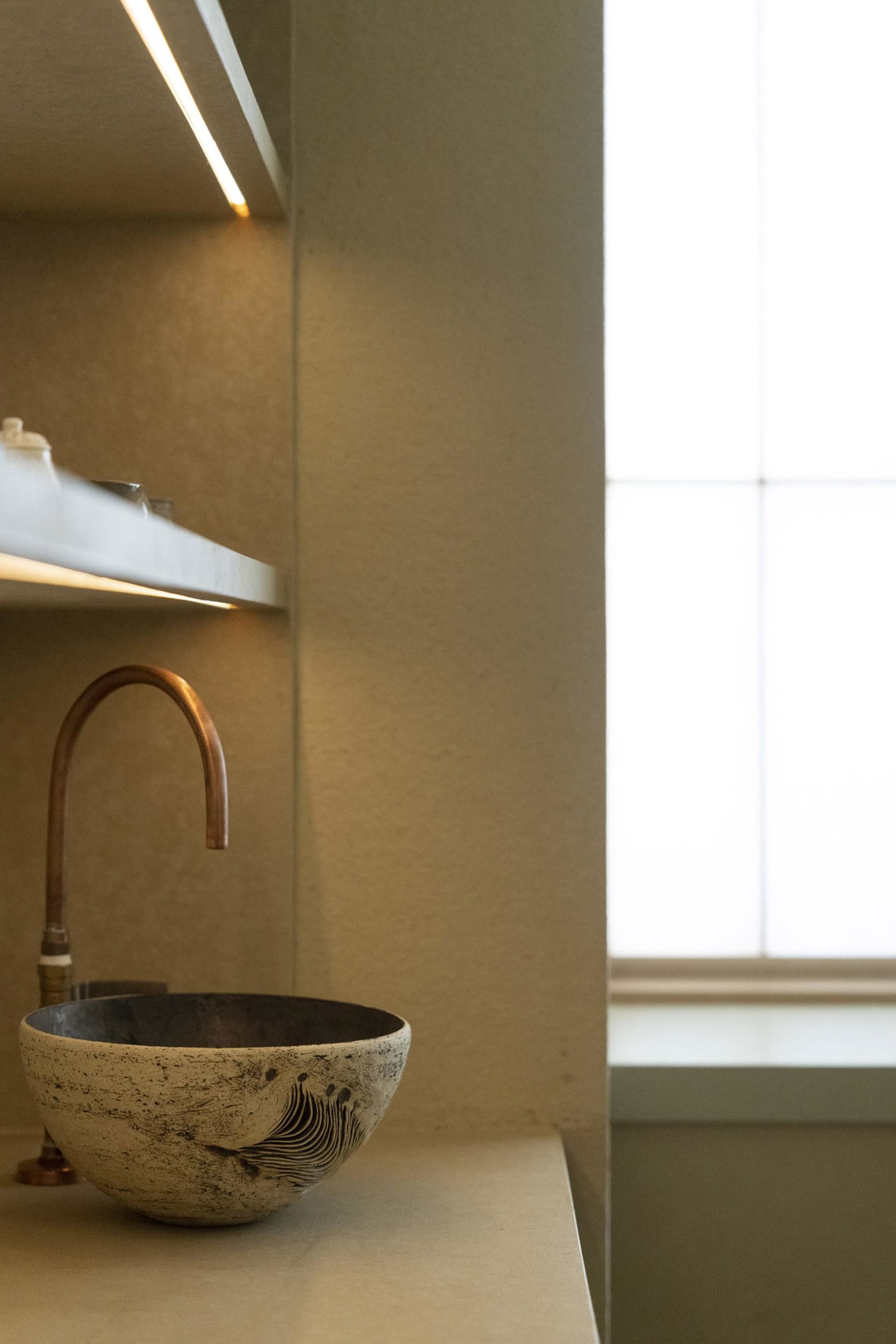 A minimalist bathroom featuring a concrete and marble sink with a curved faucet.