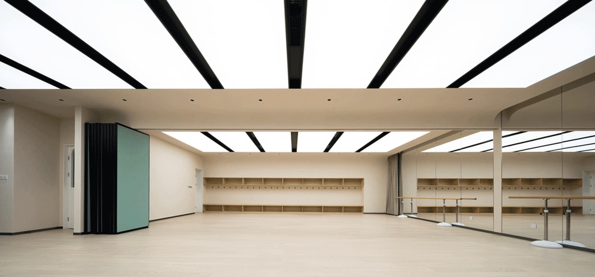 An empty minimalist dance studio with wood and glass walls, floor-to-ceiling mirrors, and black trusses on the ceiling.
