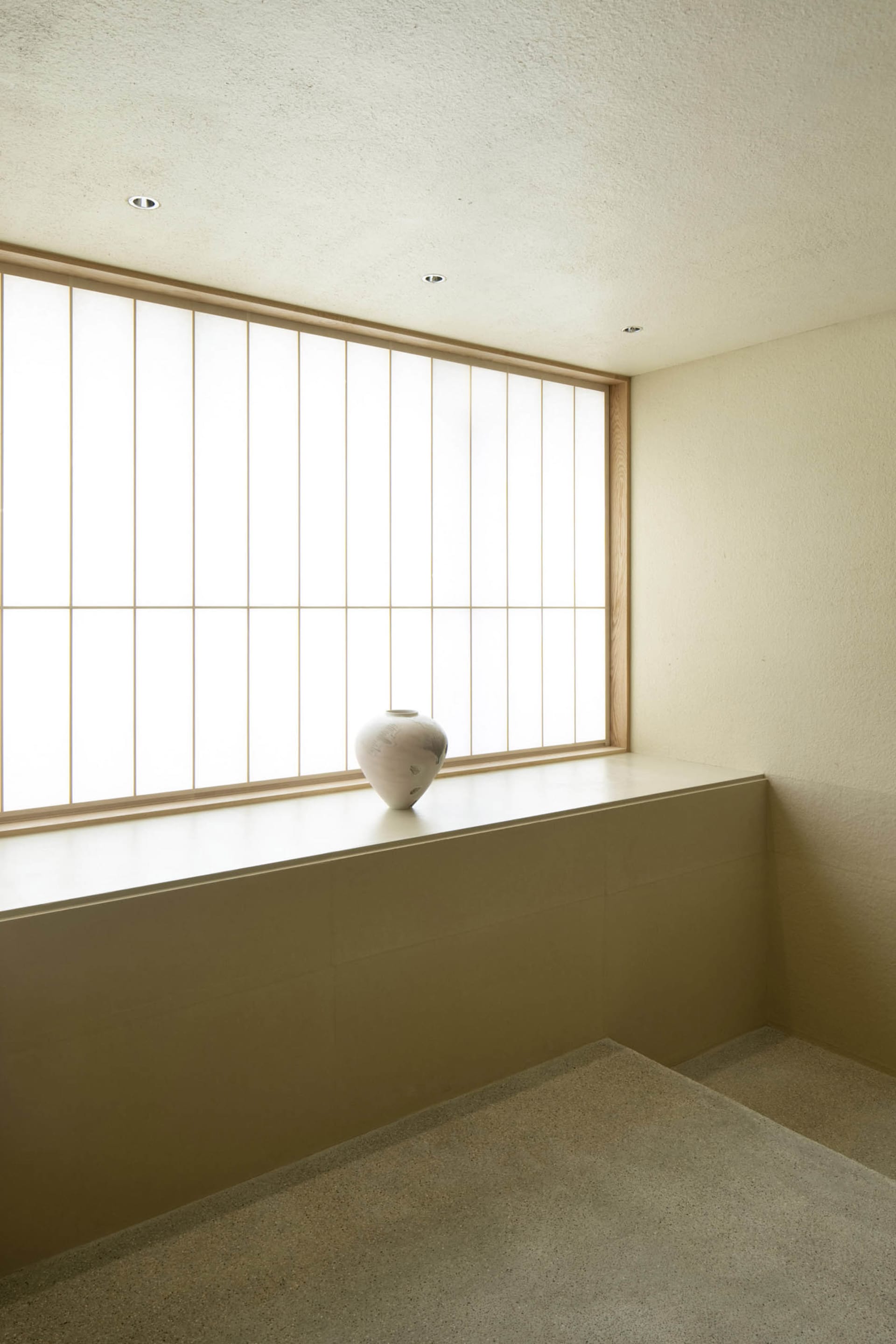 A minimalist indoor space featuring a white ceramic urn on a ledge with a large window.