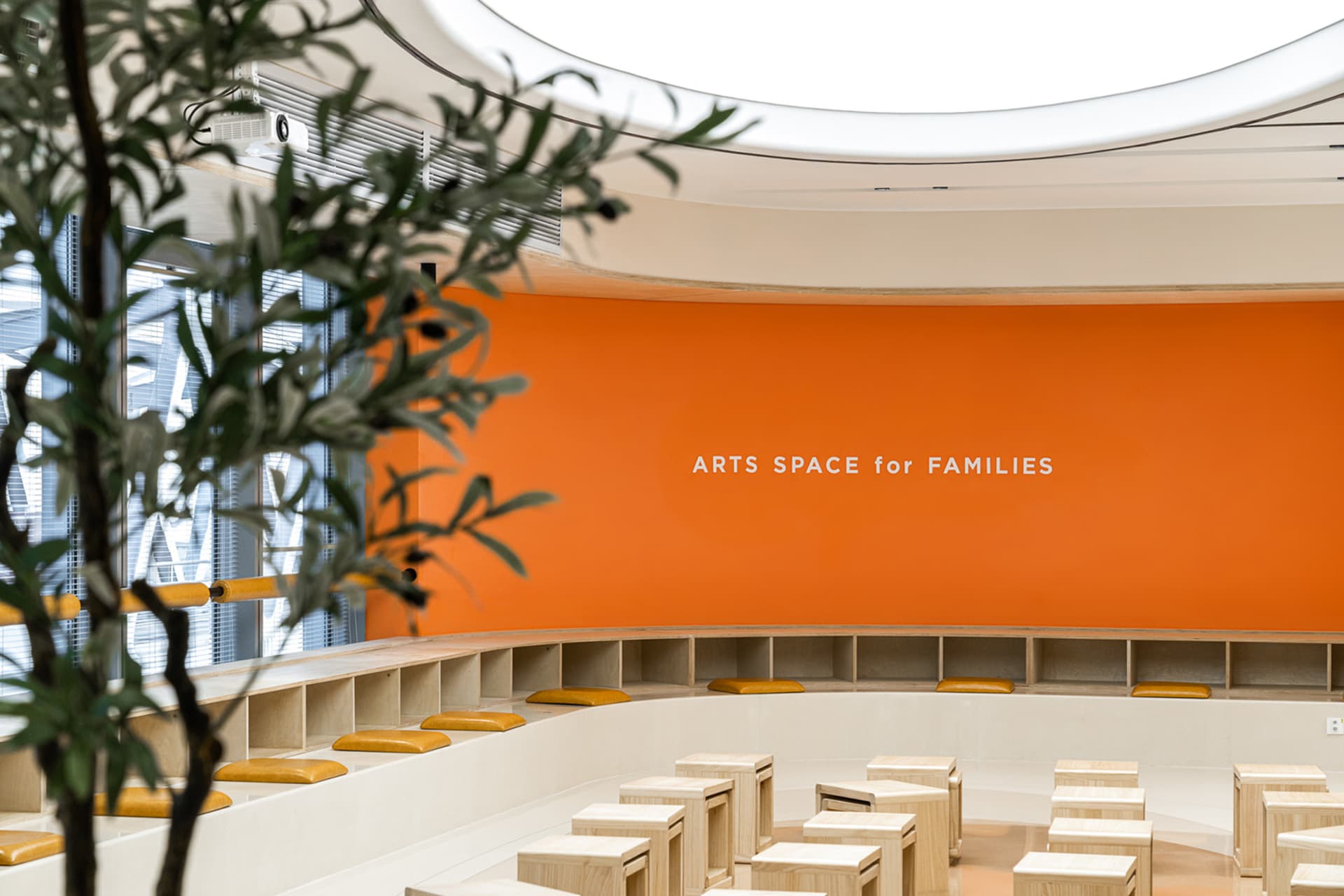 A modern interior design featuring an orange wall with the text 'ARTS SPACE for FAMILIES' and various seating arrangements.