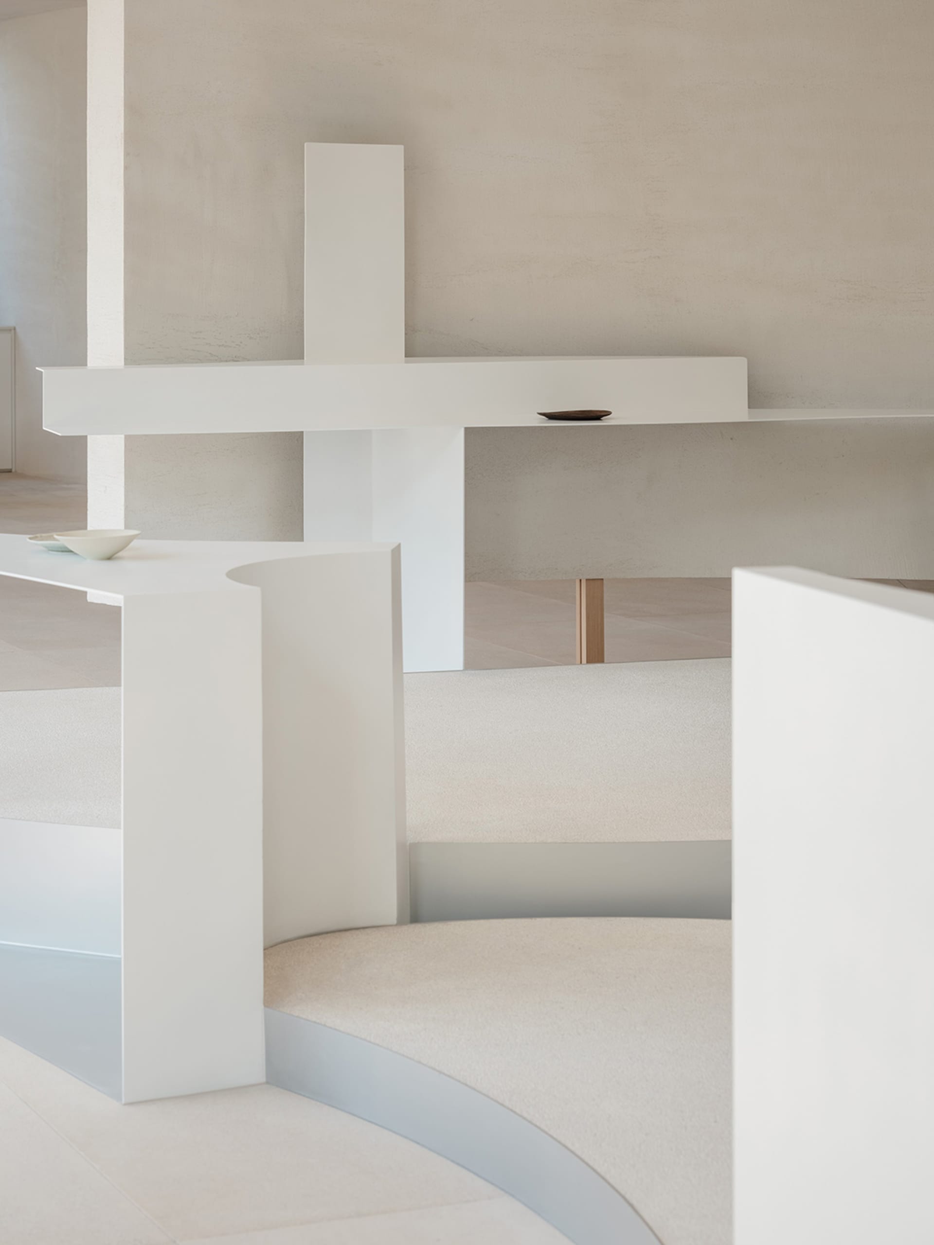 A minimalist interior space with white and concrete elements, featuring a curved staircase and minimal decor.