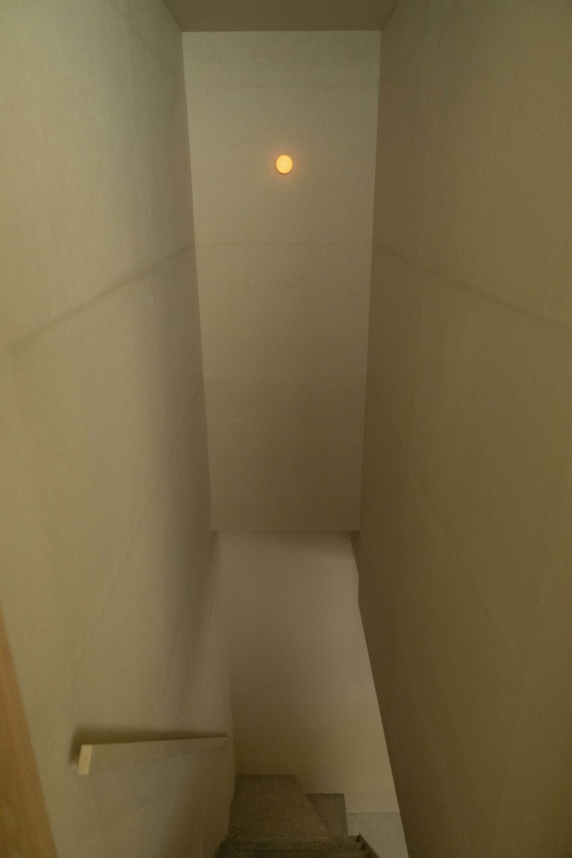 A minimalist staircase made of concrete and glass, illuminated by a singular light source.