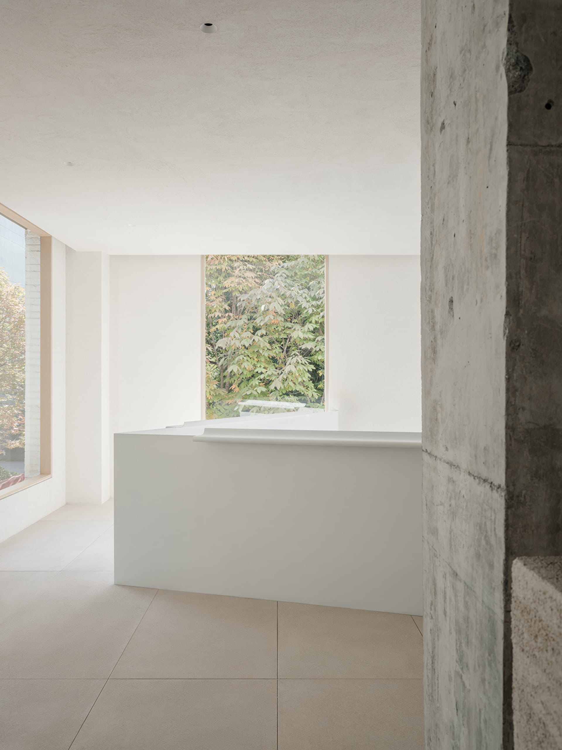 A modern reception area with a minimalist design, featuring concrete materials and a sleek, white desk.