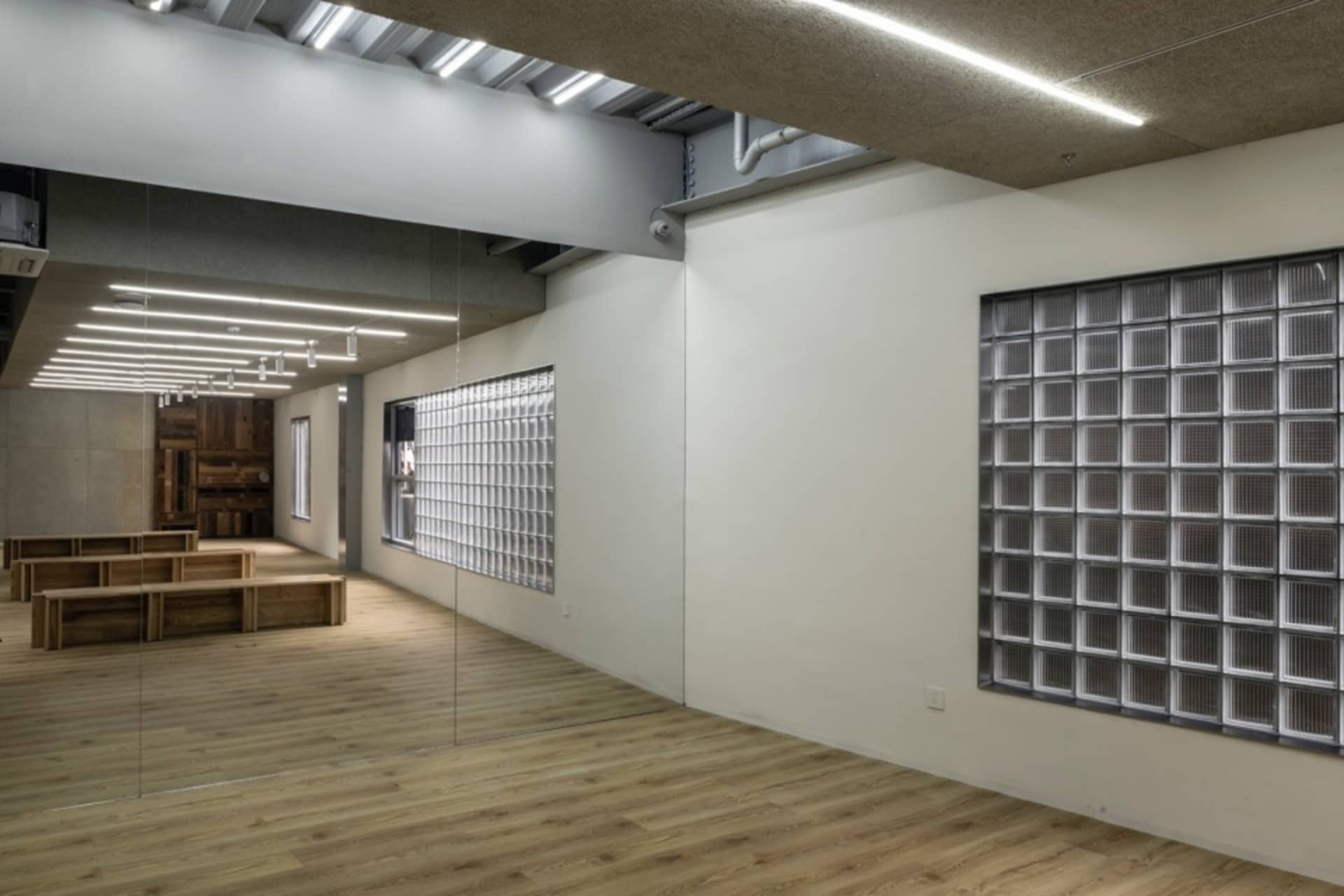 A minimalist workout room with glass blocks and wooden benches under bright lighting.