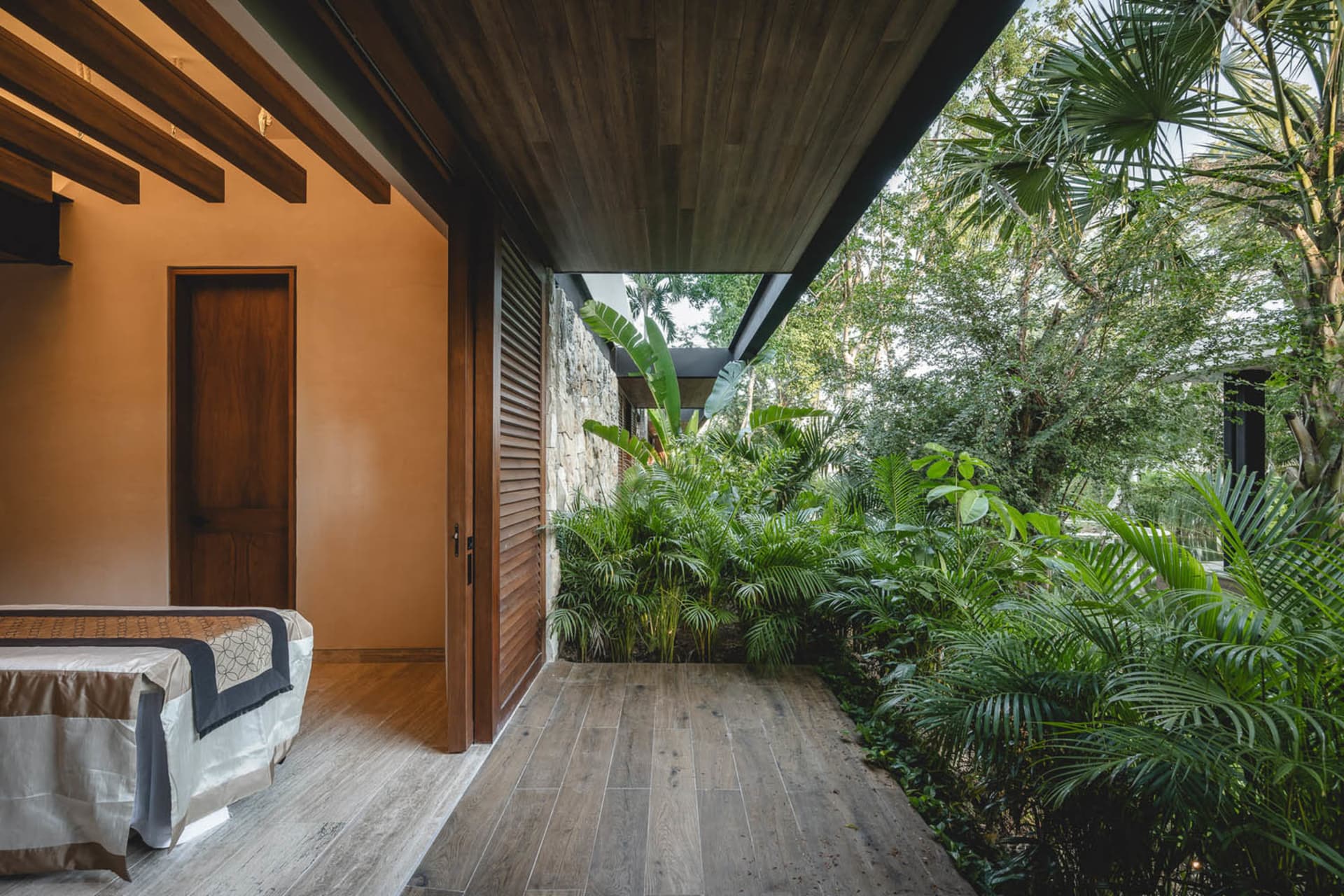 A modern bedroom with wooden walls, hardwood floors, and lush green plants.