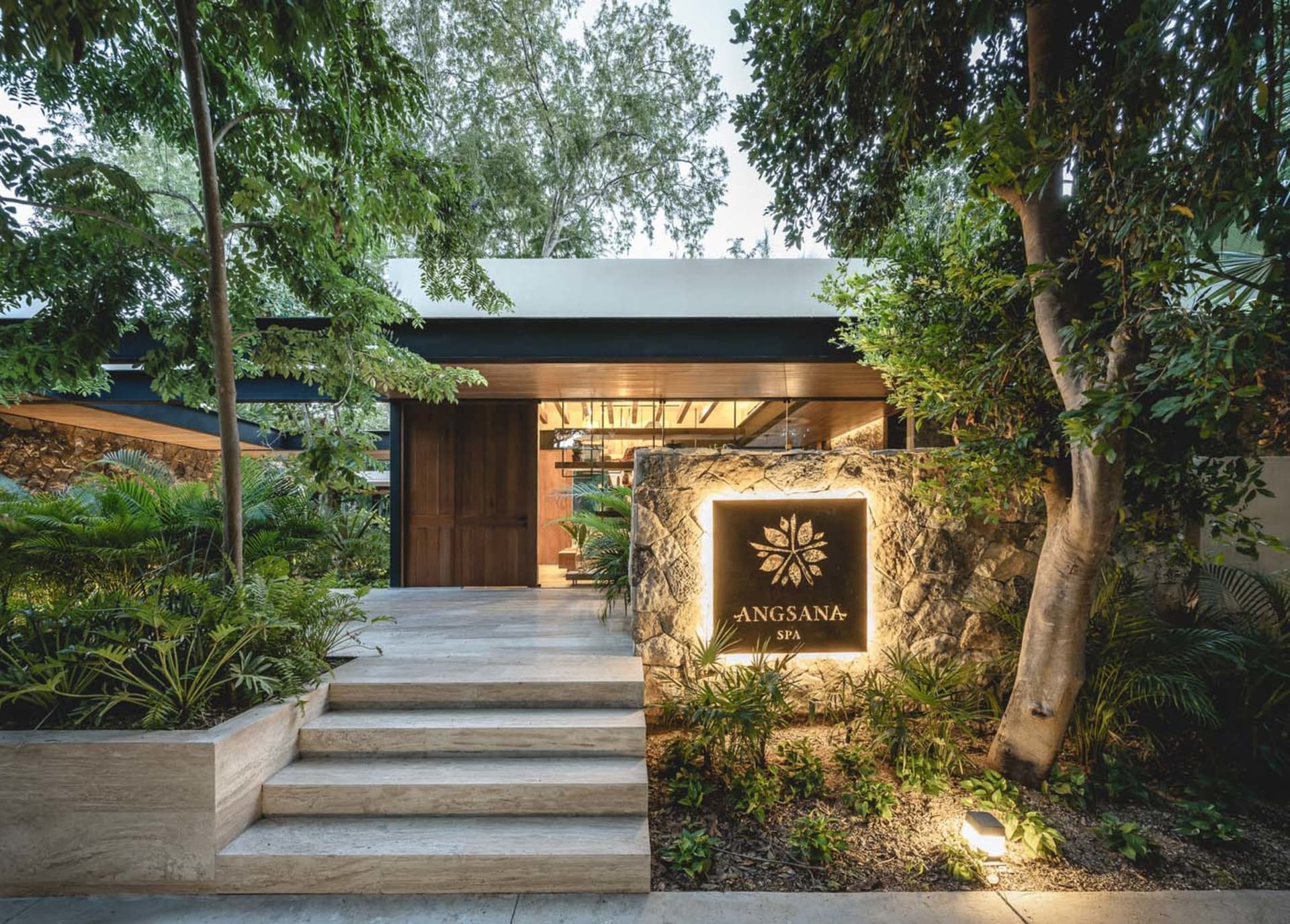 An illuminated stone sign for the Angsana Spa, set within lush greenery, featuring clean contemporary lines and a minimalist