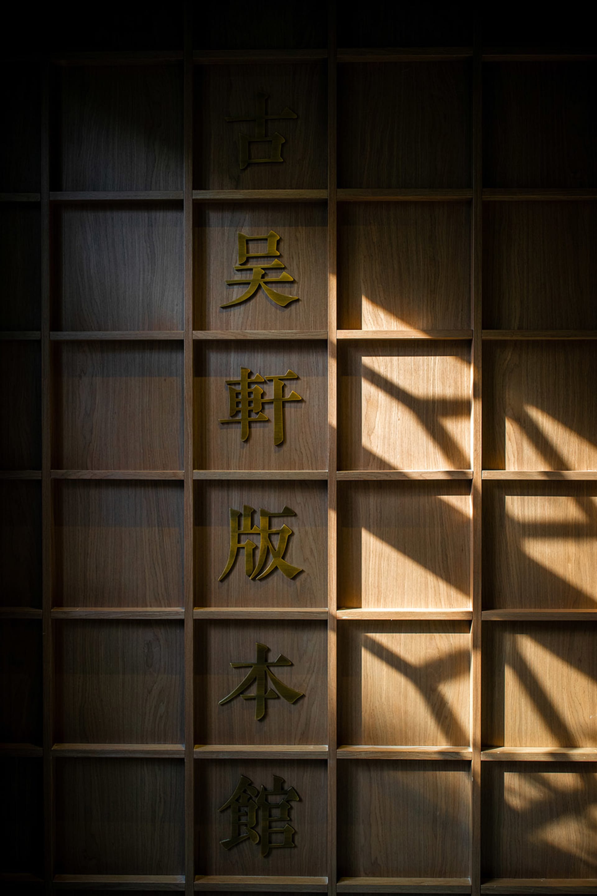 木質書櫃上以金色日文文字在深色背景中格外醒目，陽光穿透而入。