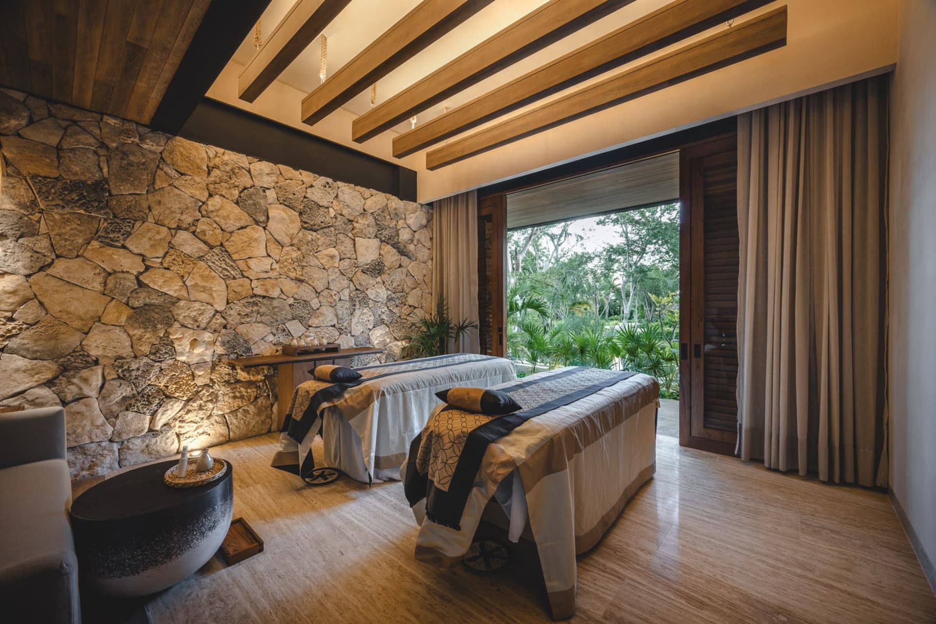 A modern spa suite featuring stone and wood materials, with a view of lush greenery outside.