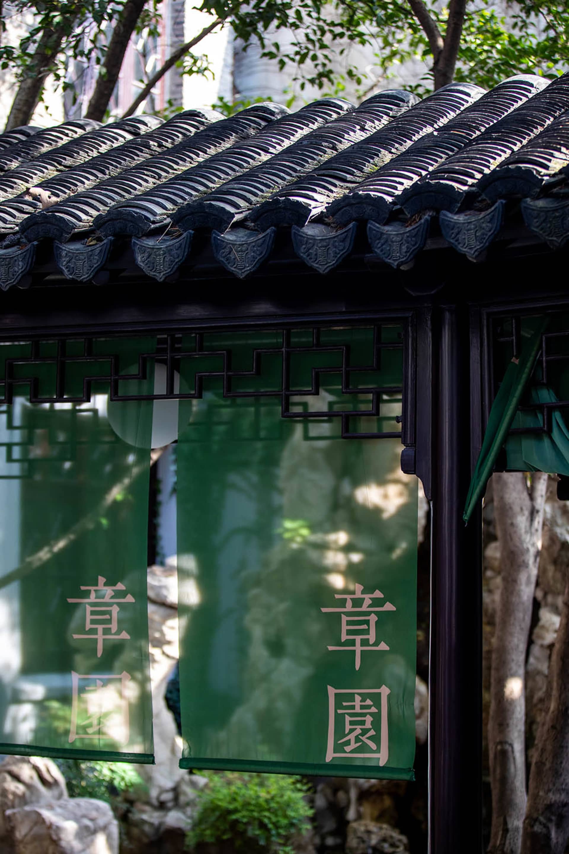 Green cloth with Chinese characters hanging from a traditional Chinese garden pavilion.