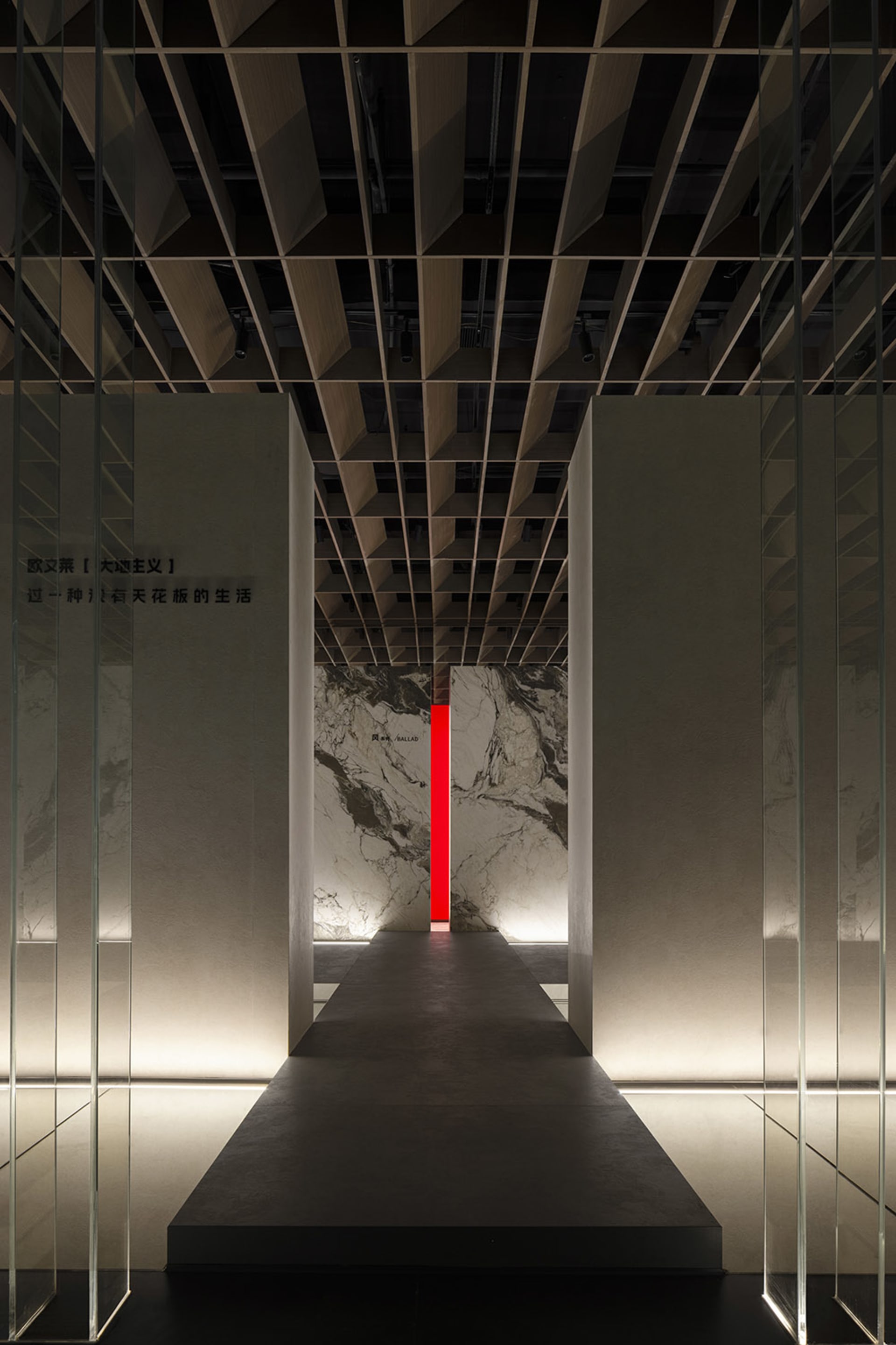 View down a minimalist hallway in an exhibition space, featuring stone walls.