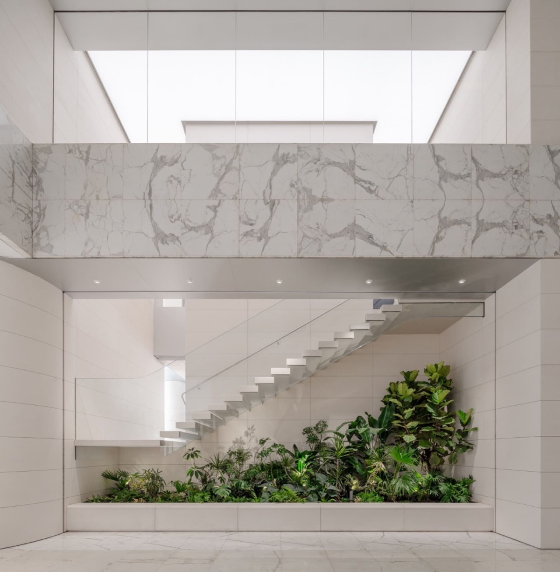 A modern and minimalist interior space with marble walls and floors, featuring a glass ceiling and green plants.