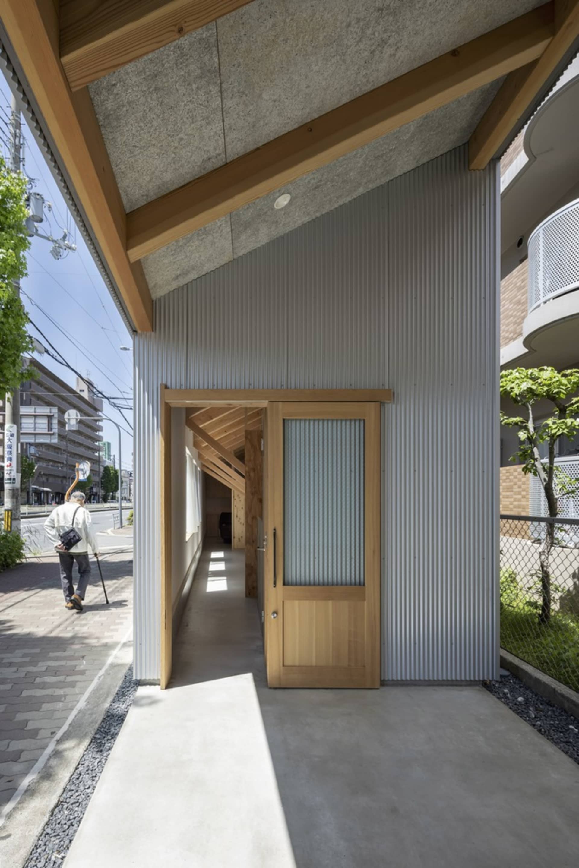 Concrete sidewalk, metal siding, wooden door with glass insert, and concrete exterior wall