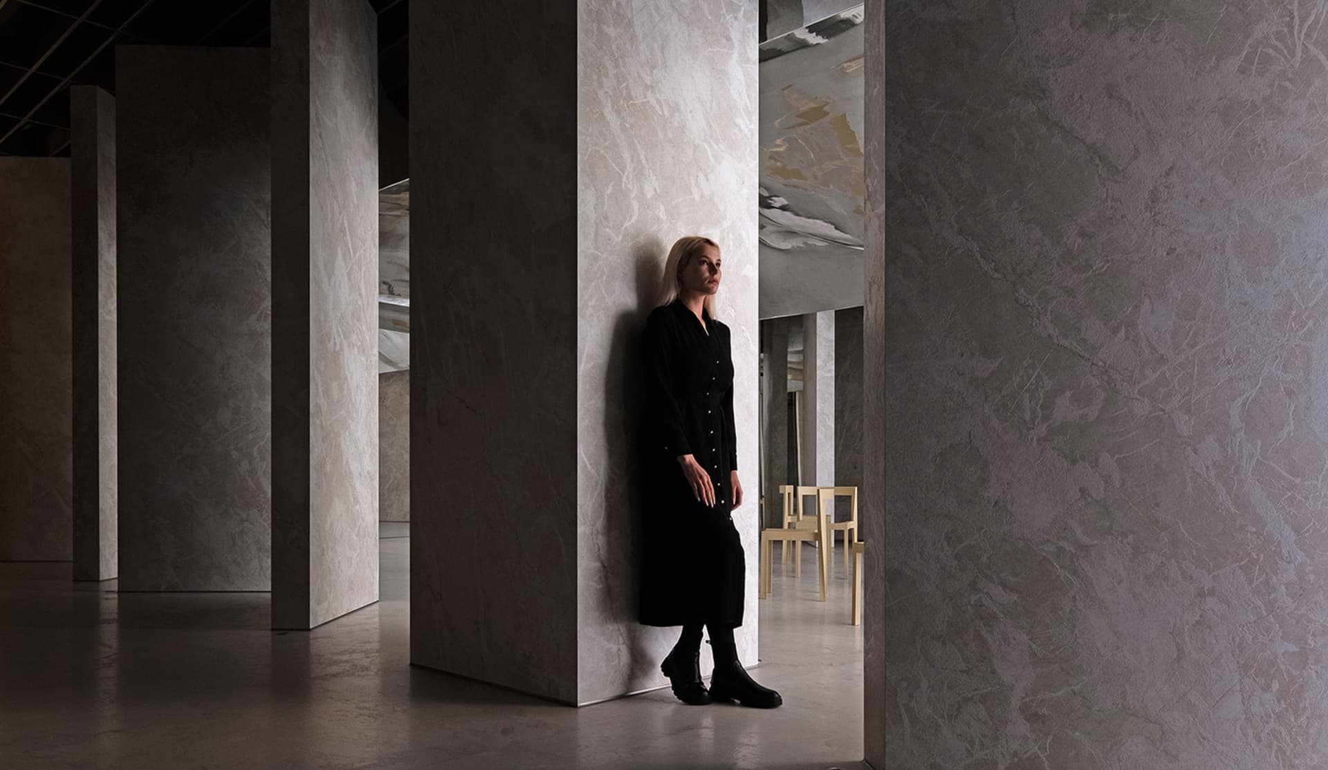 A person standing in a minimalist interior with concrete walls.