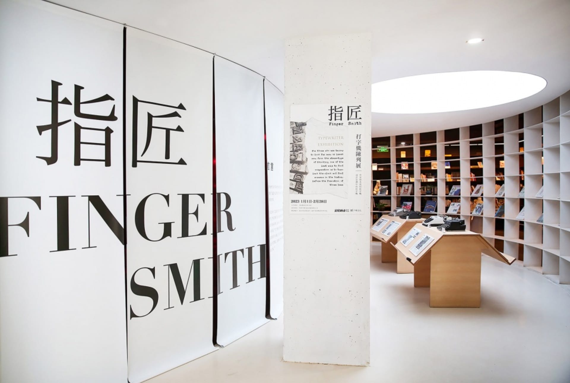 現代白色烤漆鋼製圖書館室內，書架上擺滿書籍，中央有弧形牆面，以及一盞燈具